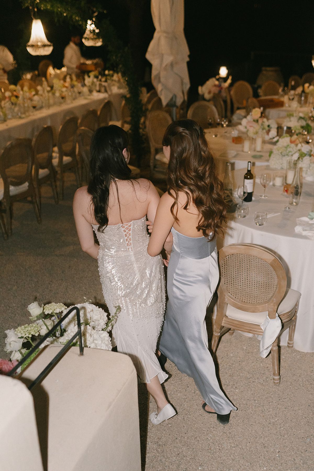 Two women in evening dresses walking between the dinner tables at night