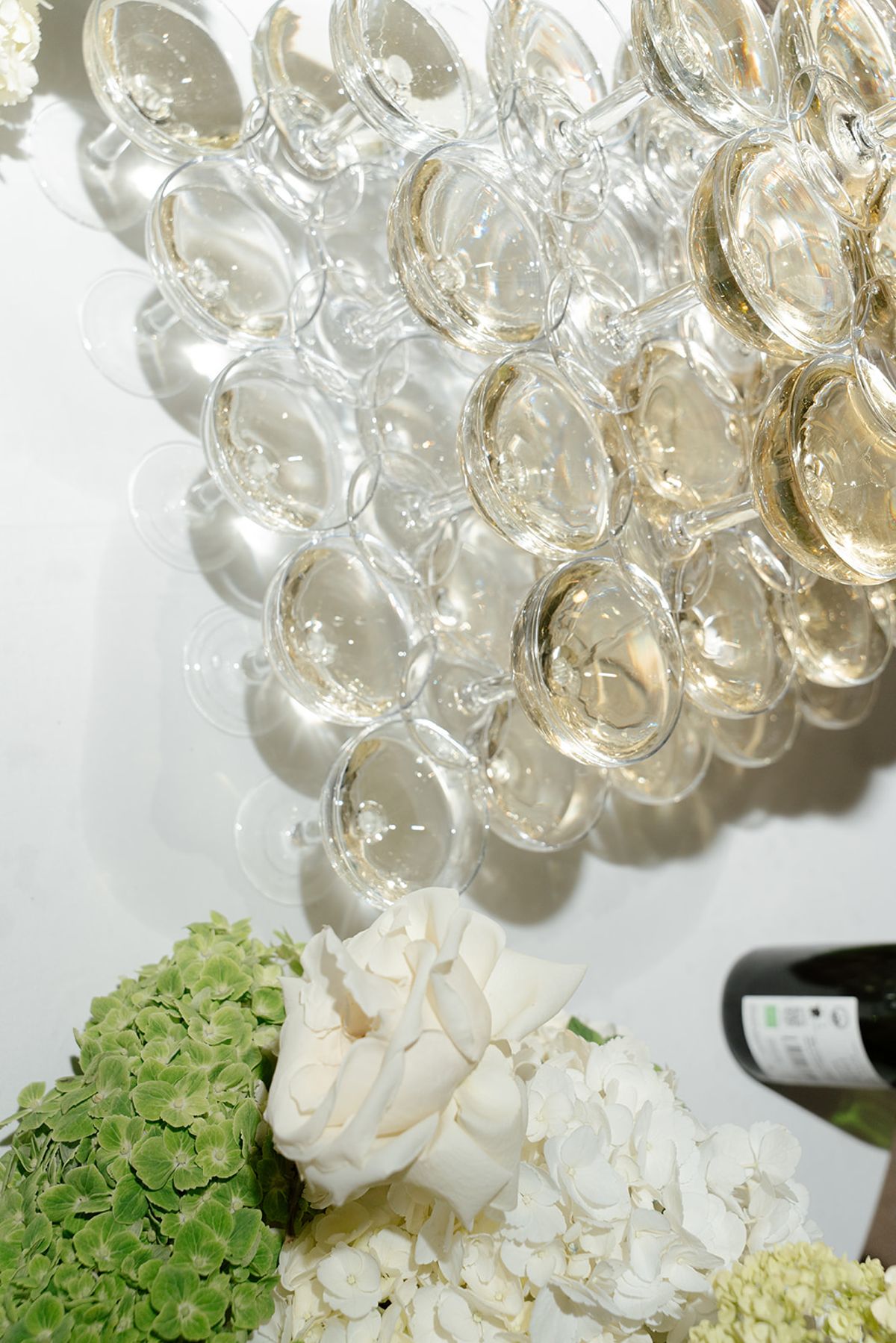 Champagne being poured into a tower of coupes above white hydrangea