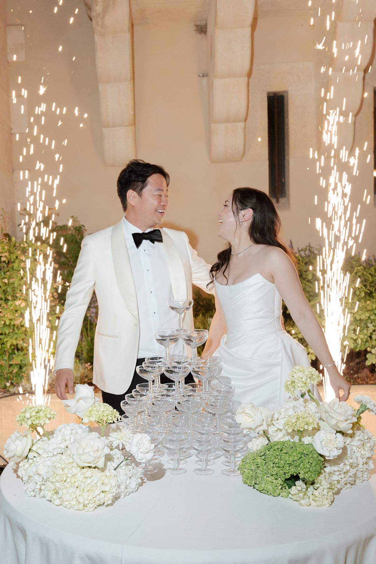 Carina and Stefan beside the champagne tower as sparklers fire behind them