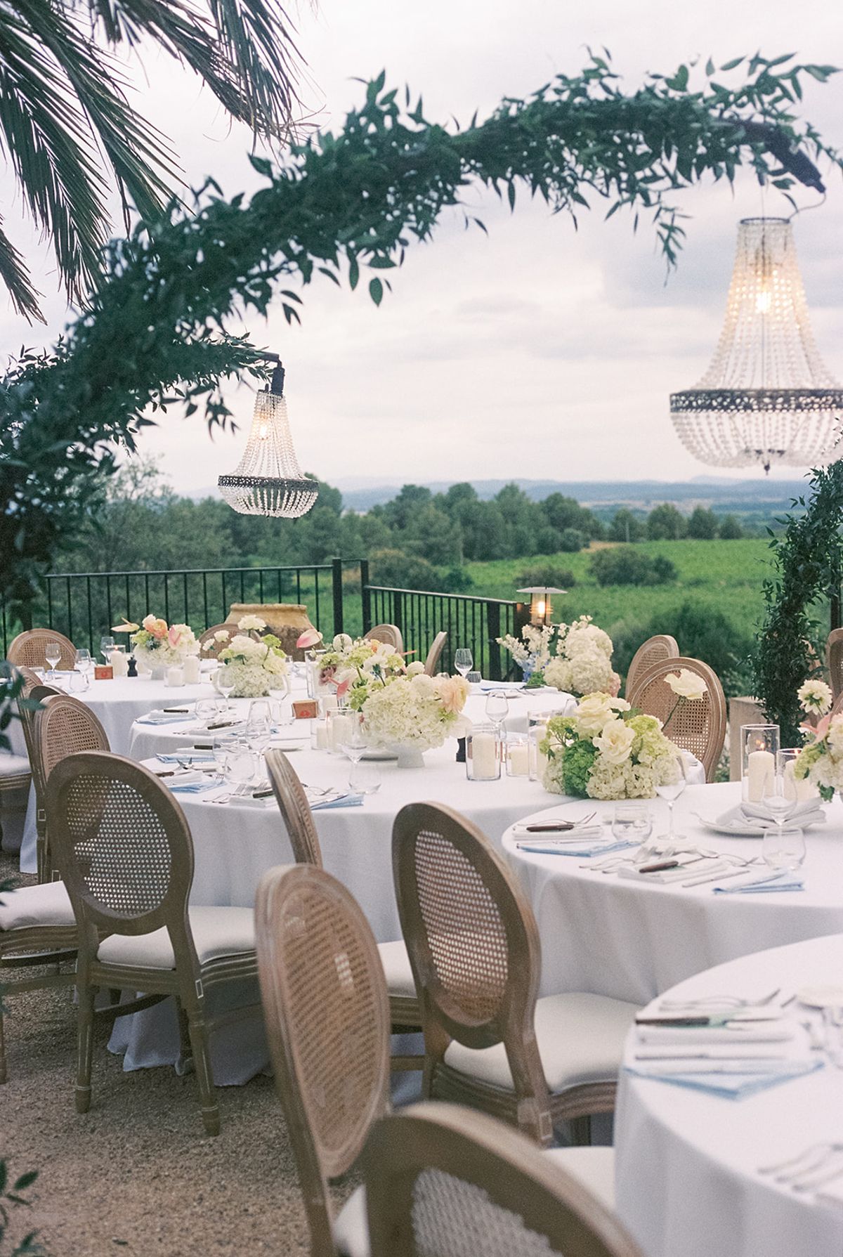 Dinner tables under a green arch hung with a crystal chandelier, vineyards beyond