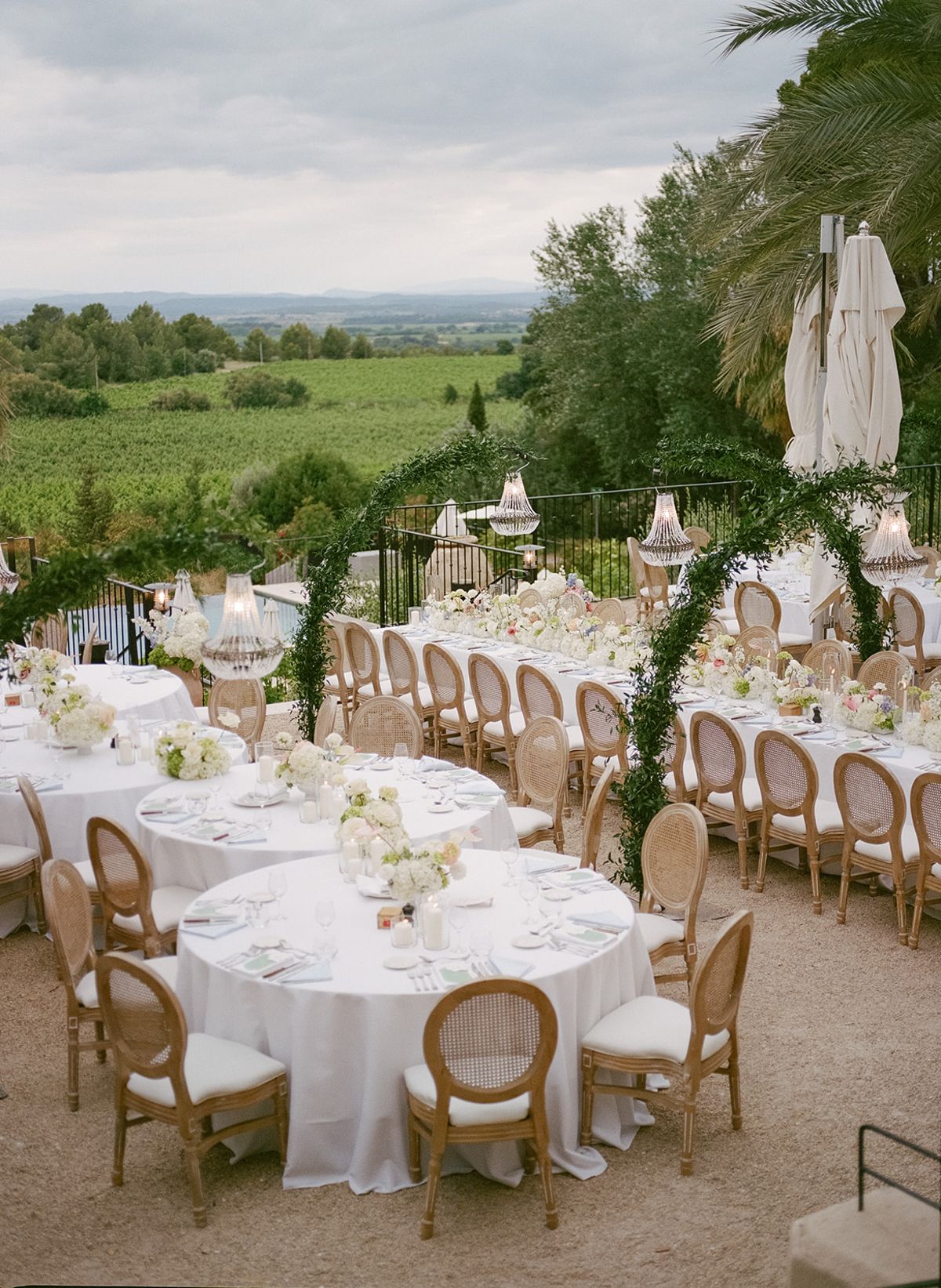 Round and long dinner tables under green arches with the vineyards beyond