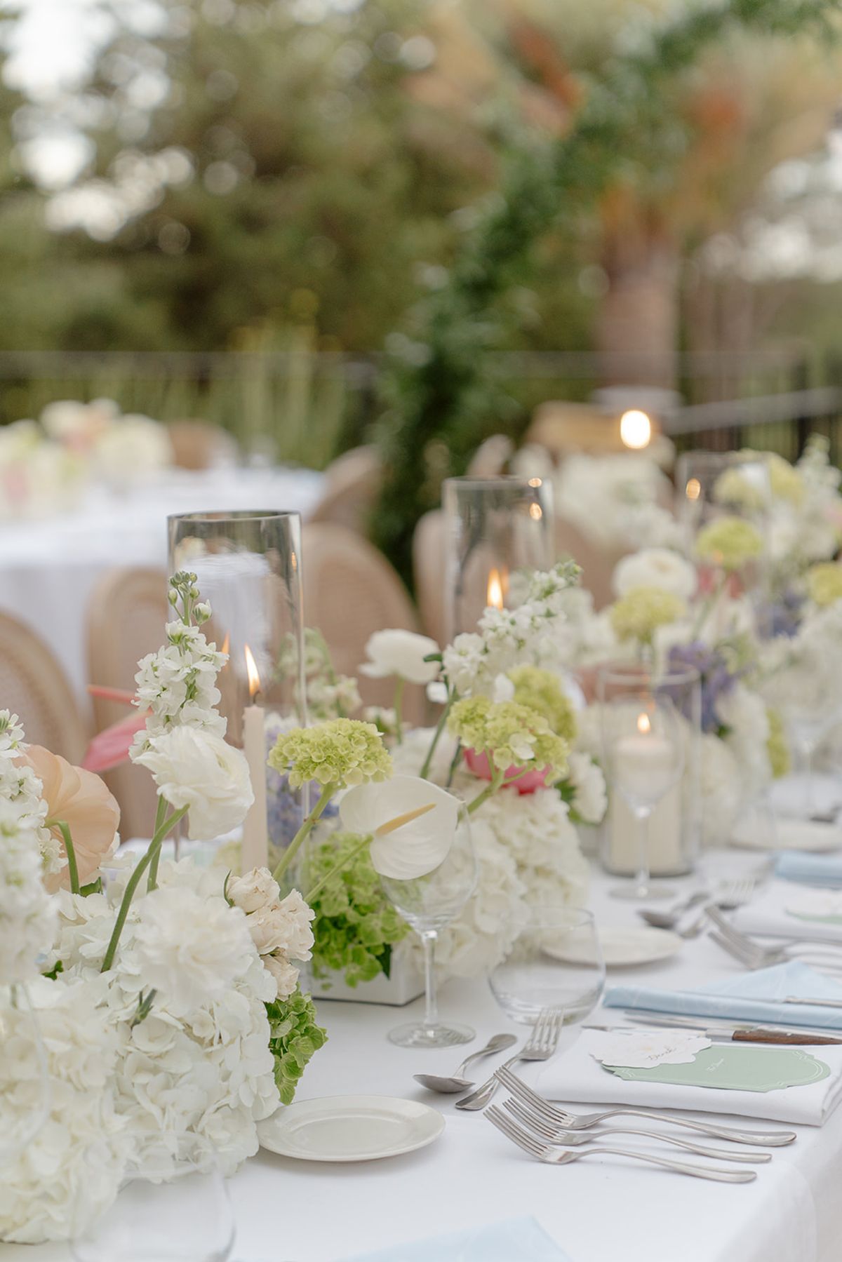 Low white and green table flowers with candles and place settings at dinner