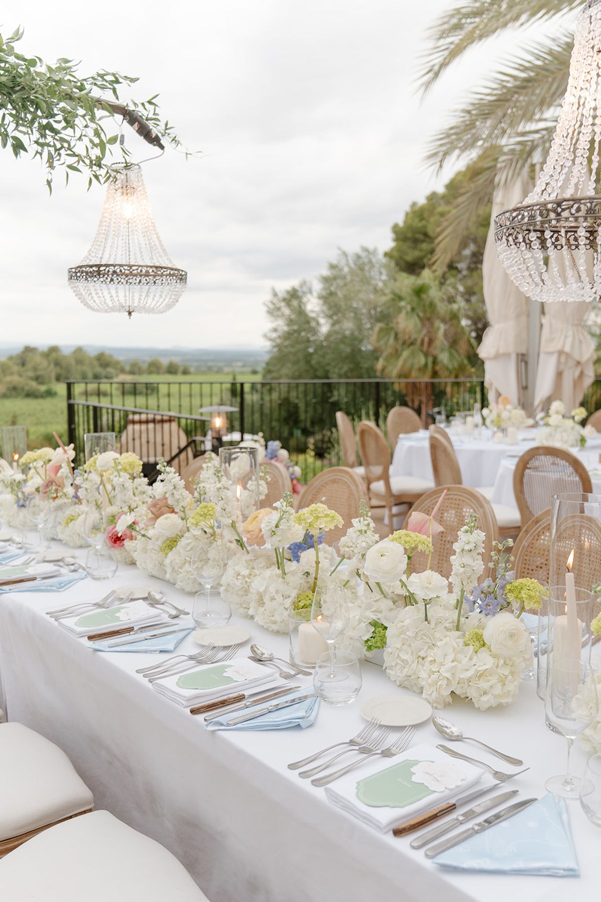 A crystal chandelier hanging from a green arch over a long dinner table facing the vineyards
