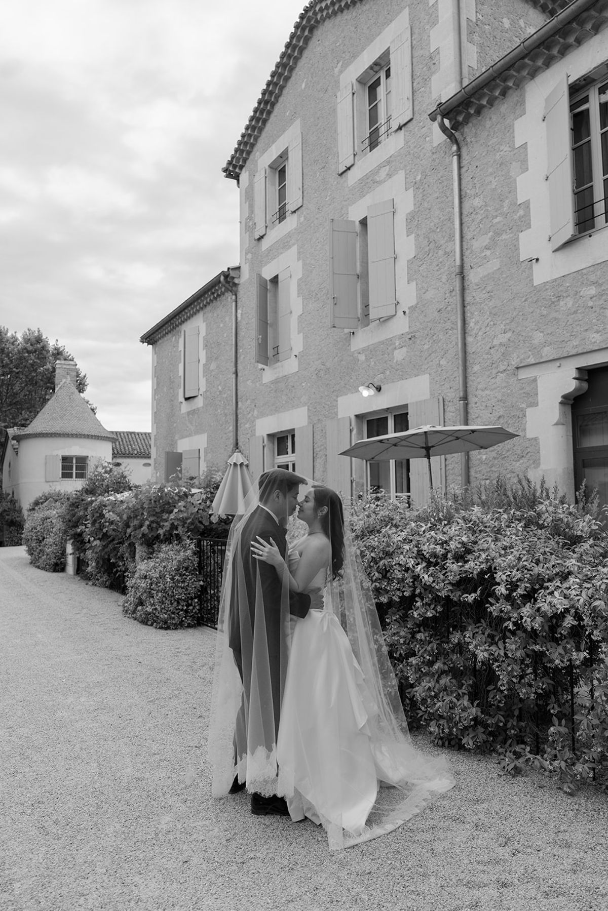 Black and white view of Carina and Stefan kissing on a gravel lane beside the estate buildings