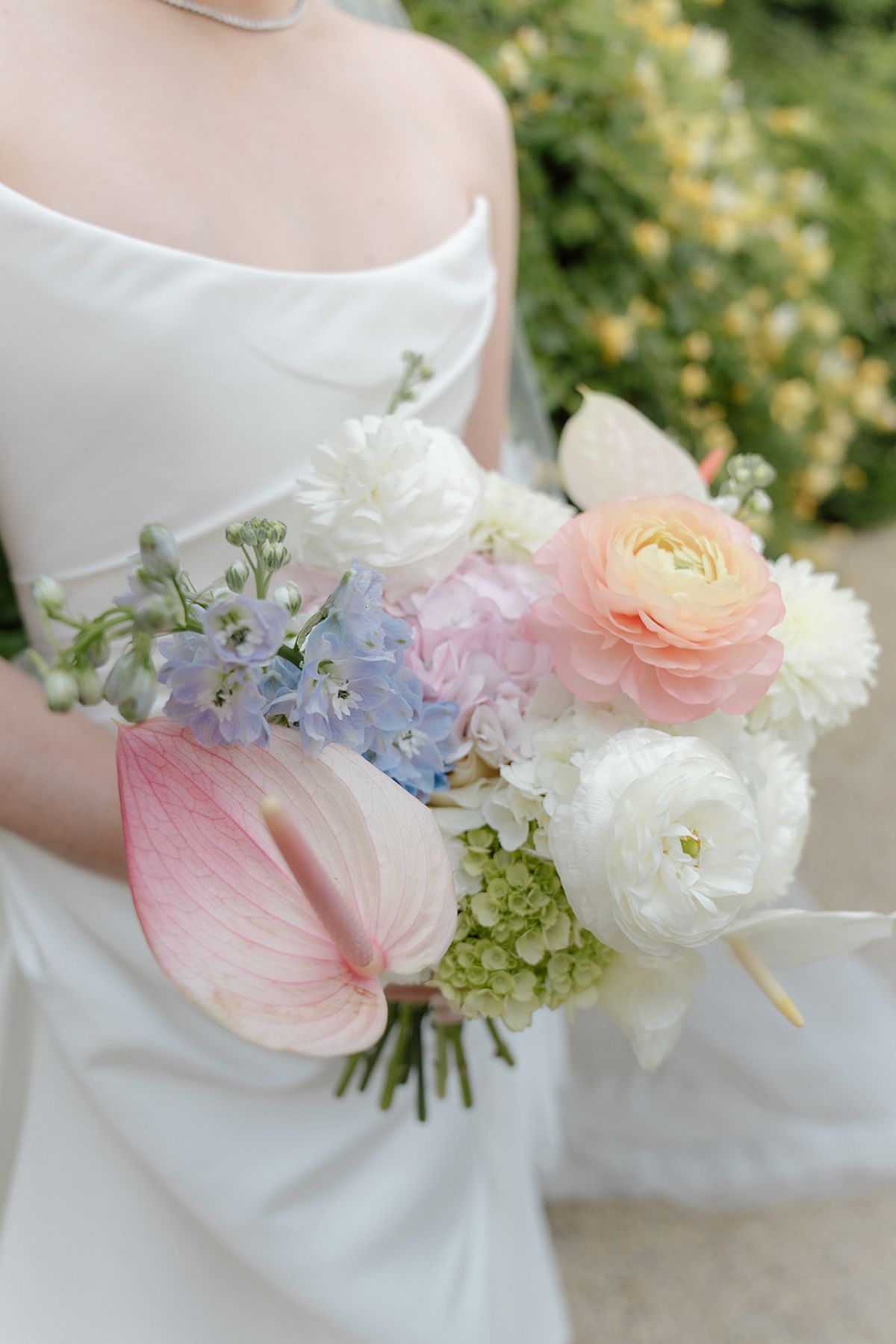 Bouquet of white ranunculus and dahlias, blue delphinium, blush anthurium and a peach ranunculus
