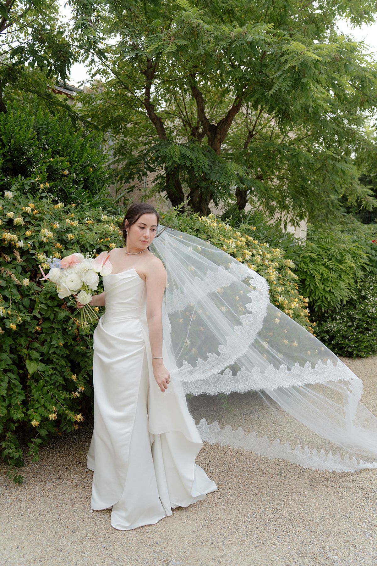 Carina holding her bouquet as her lace-trimmed veil lifts in the breeze