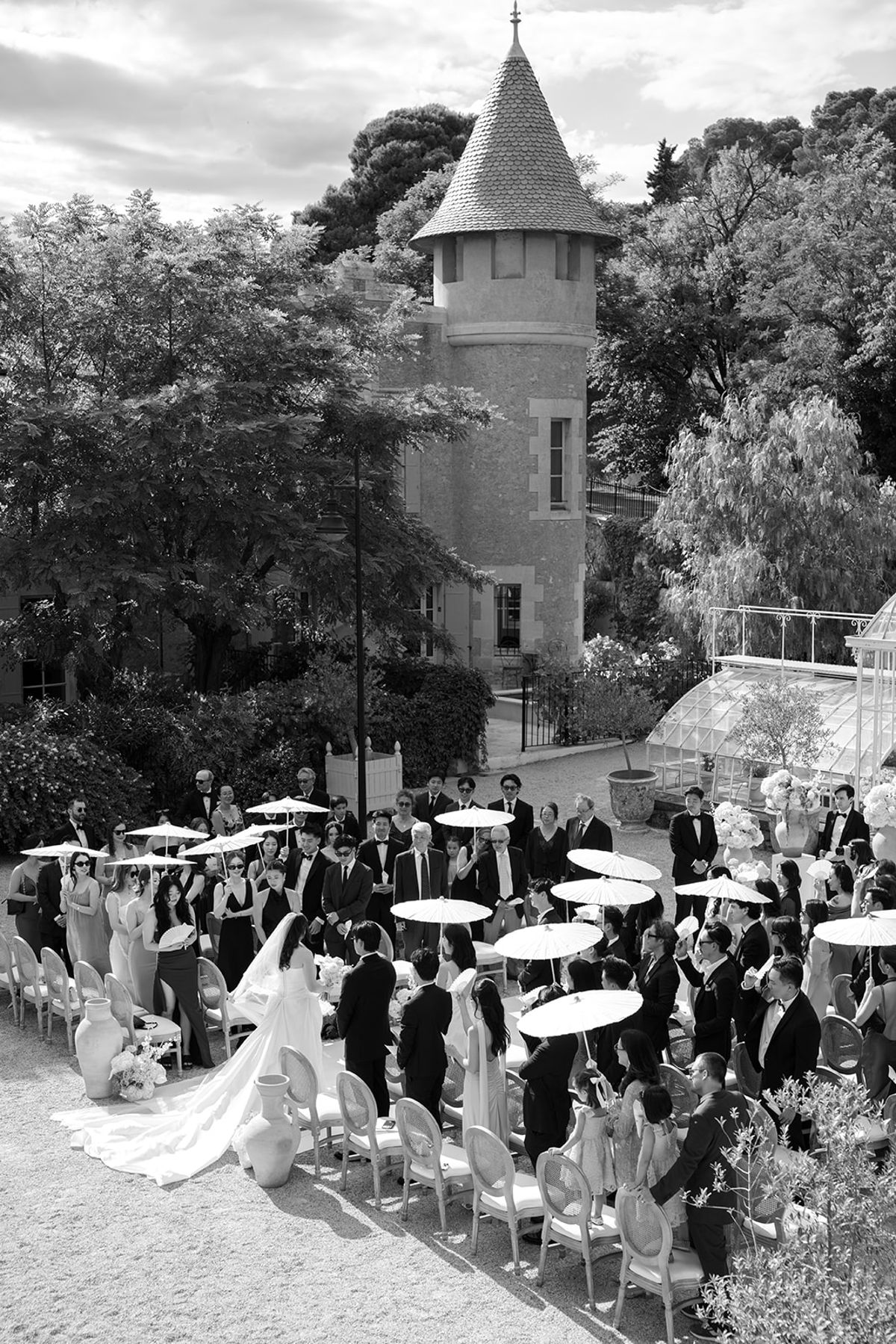 Black and white aerial view of guests under white parasols at the ceremony by the greenhouse