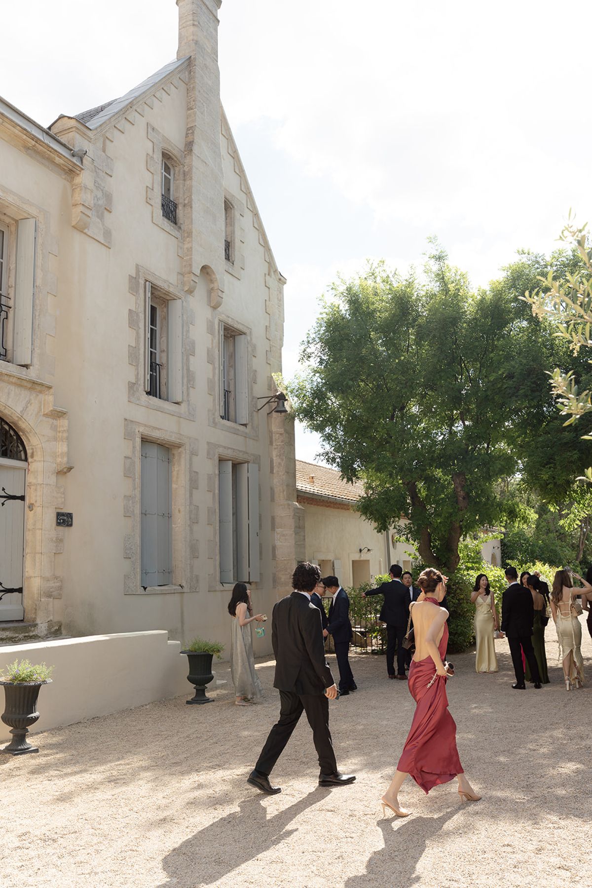 Guests in evening dress crossing the gravel courtyard of Château les Carrasses towards the ceremony