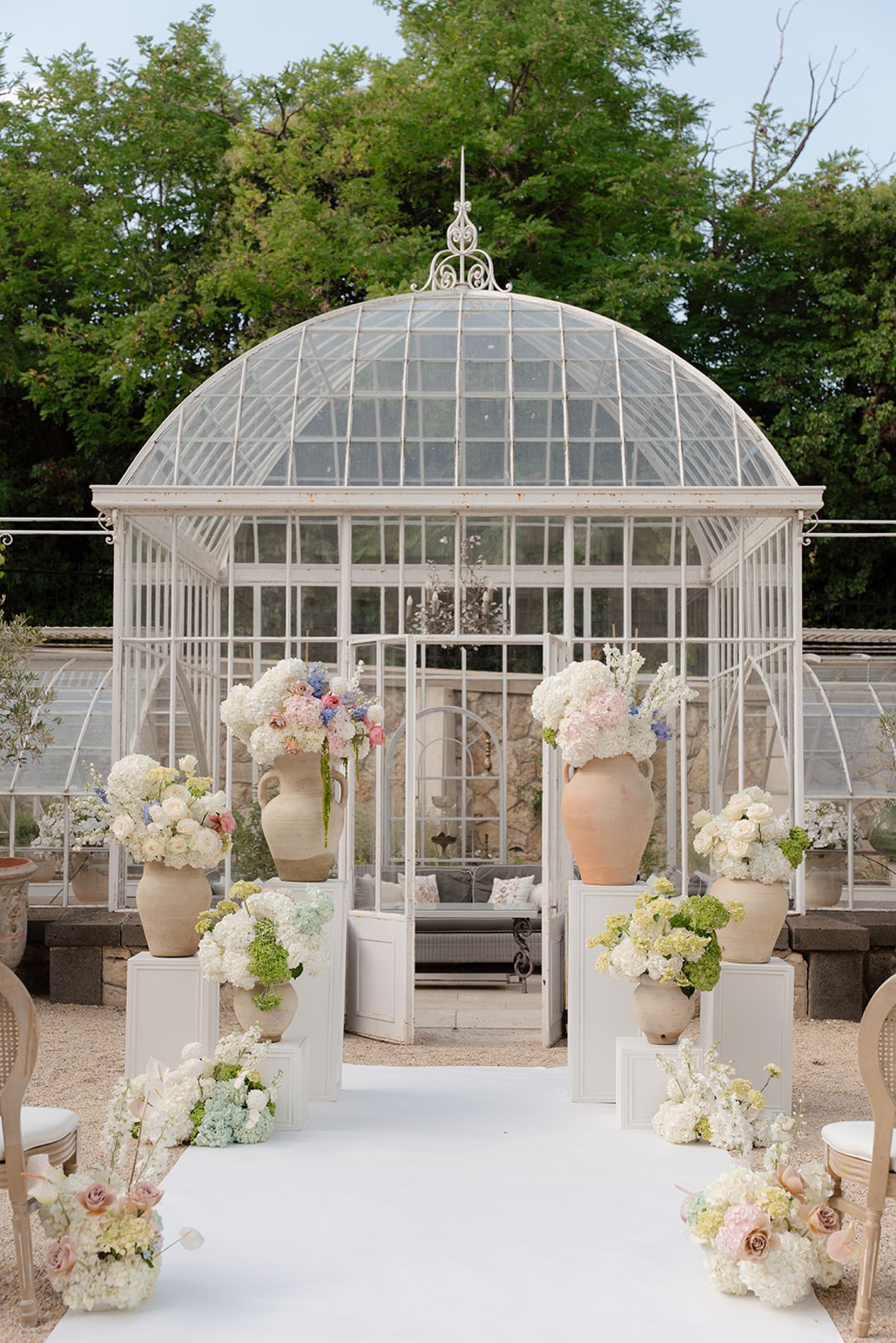 Head of the aisle before the greenhouse doors, framed by pastel flowers on white pedestals