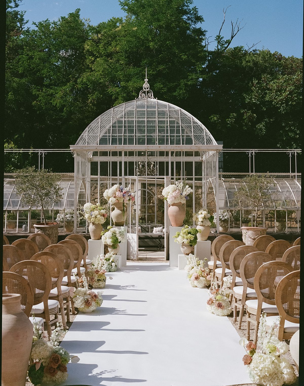 The finished ceremony aisle in front of the glass greenhouse, flanked by pastel florals