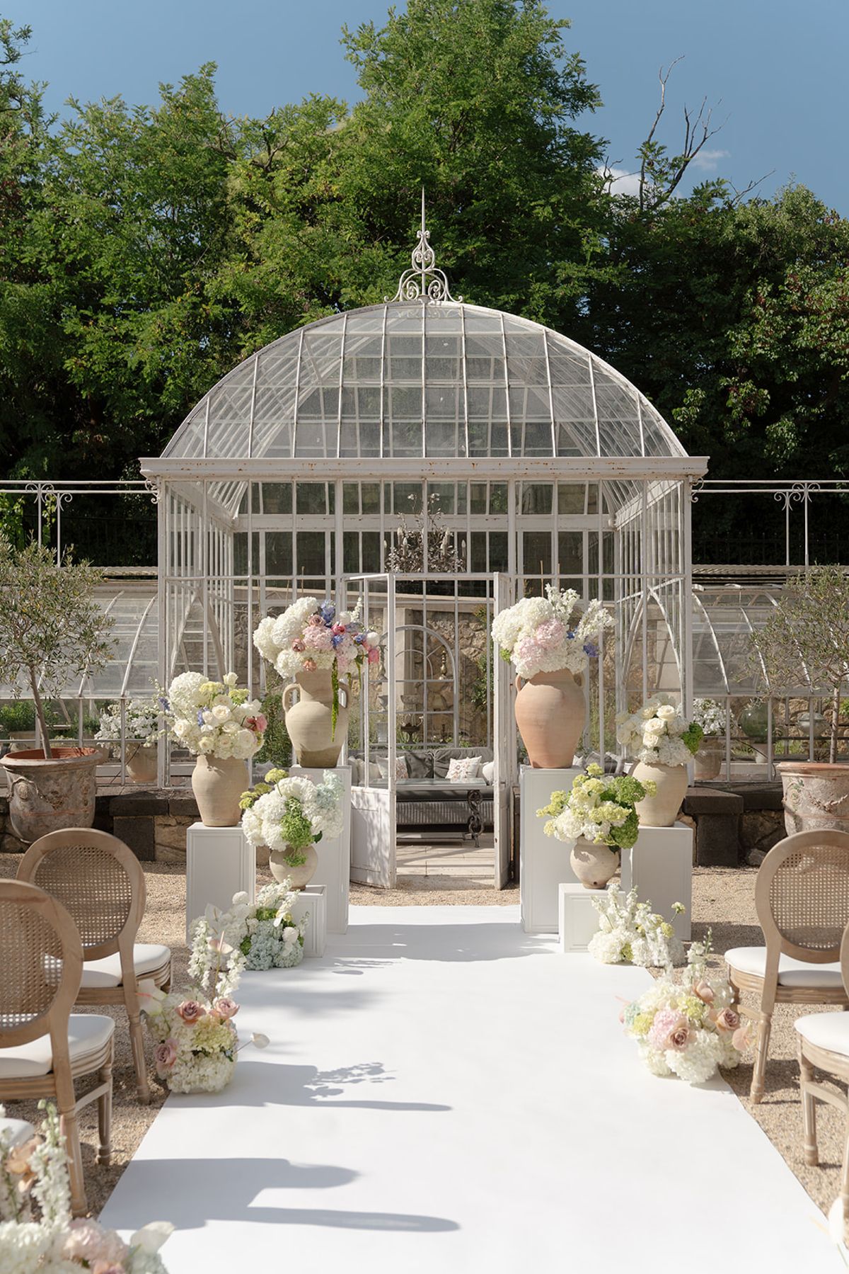 Pastel florals on white pedestals flanking the greenhouse doors at the head of the aisle