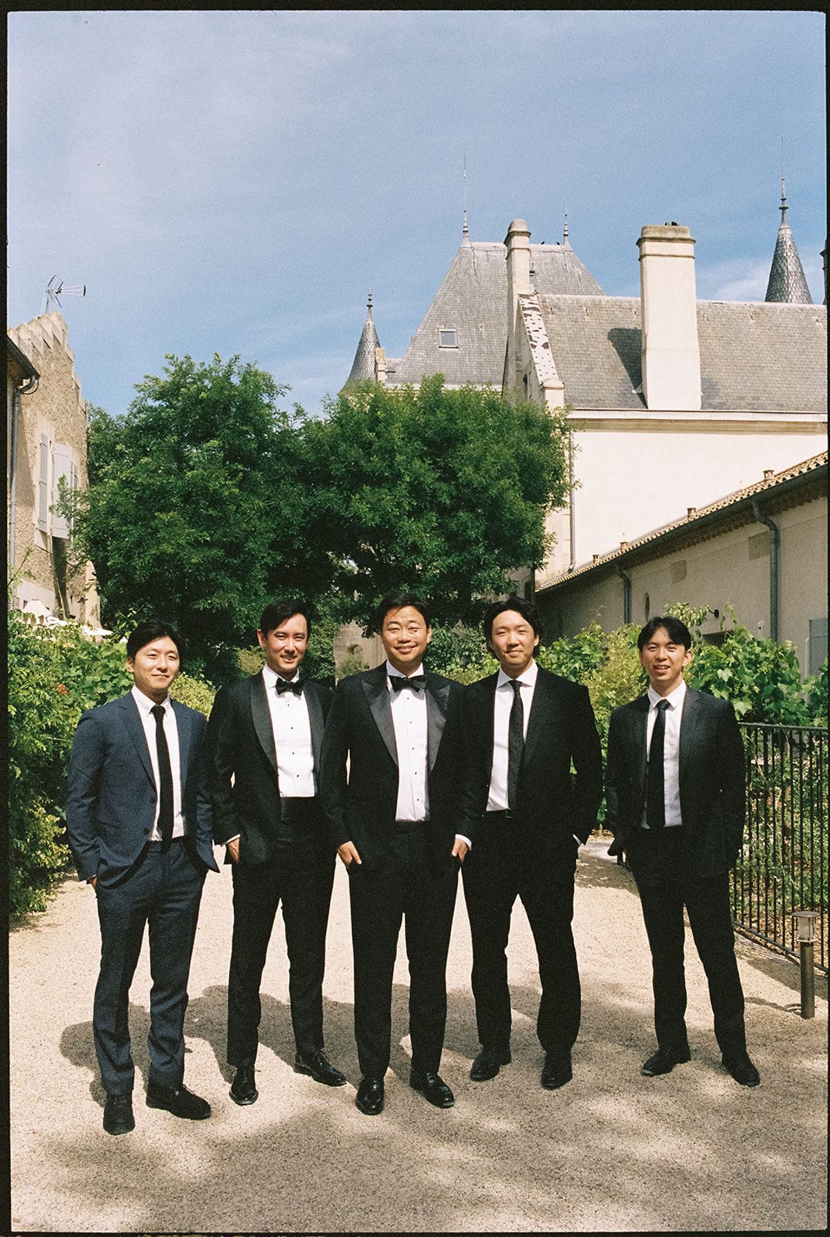 Stefan with four groomsmen, one in a tuxedo and three in dark suits, in front of Château les Carrasses