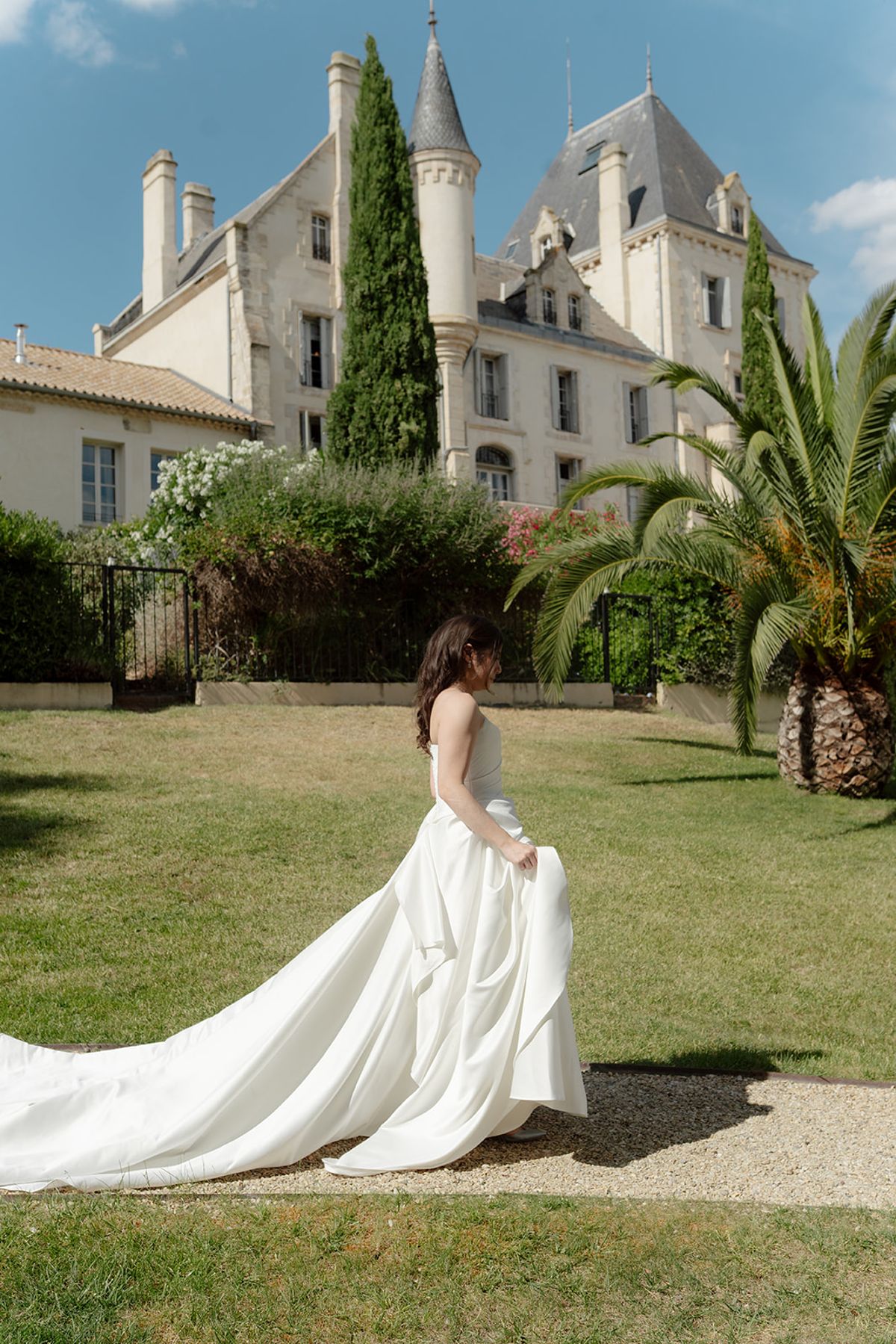 Carina in her ivory gown crossing the lawn in front of Château les Carrasses