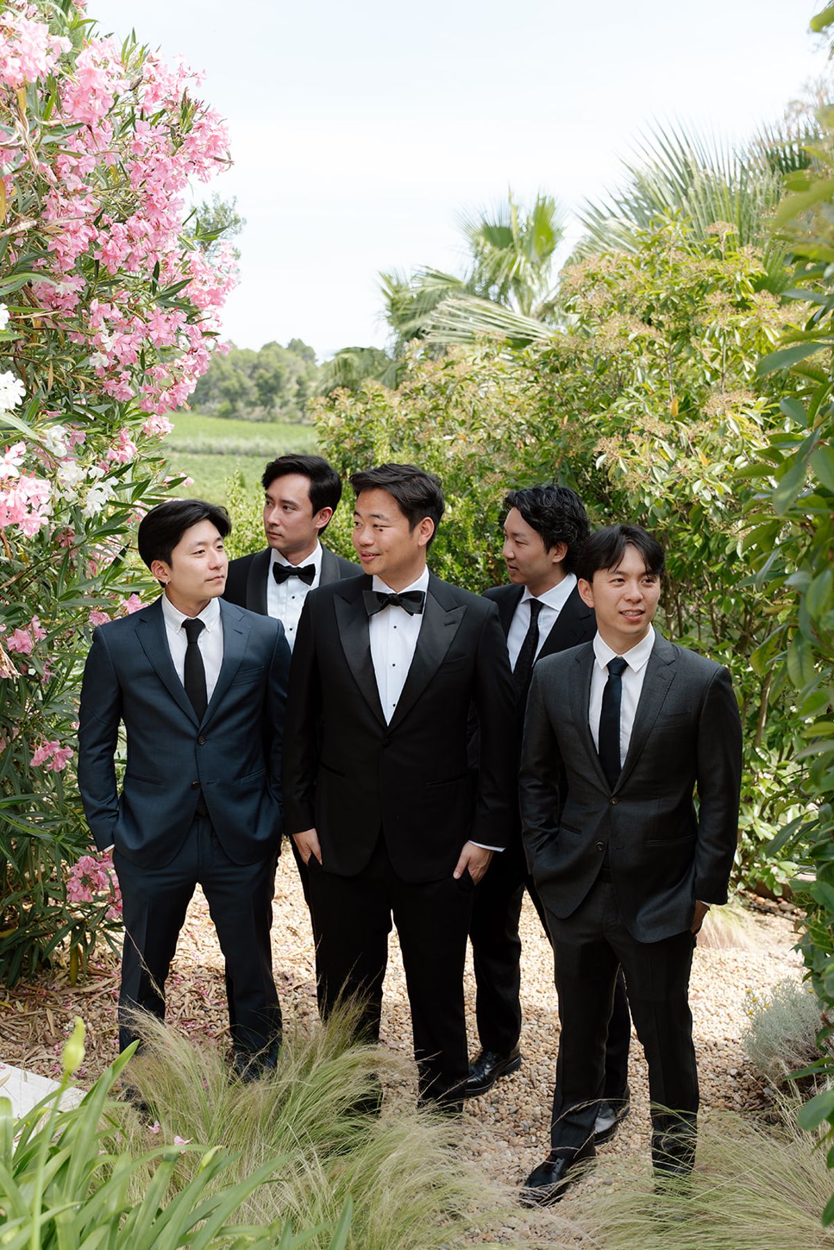 Stefan in a tuxedo with four groomsmen, one in a tuxedo and three in dark suits, beside pink oleander
