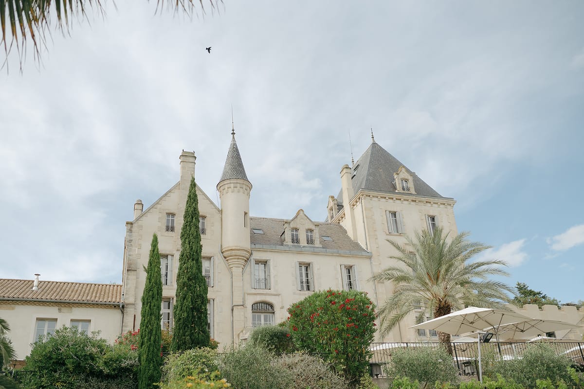 The turreted façade of Château les Carrasses behind palm trees under a pale sky