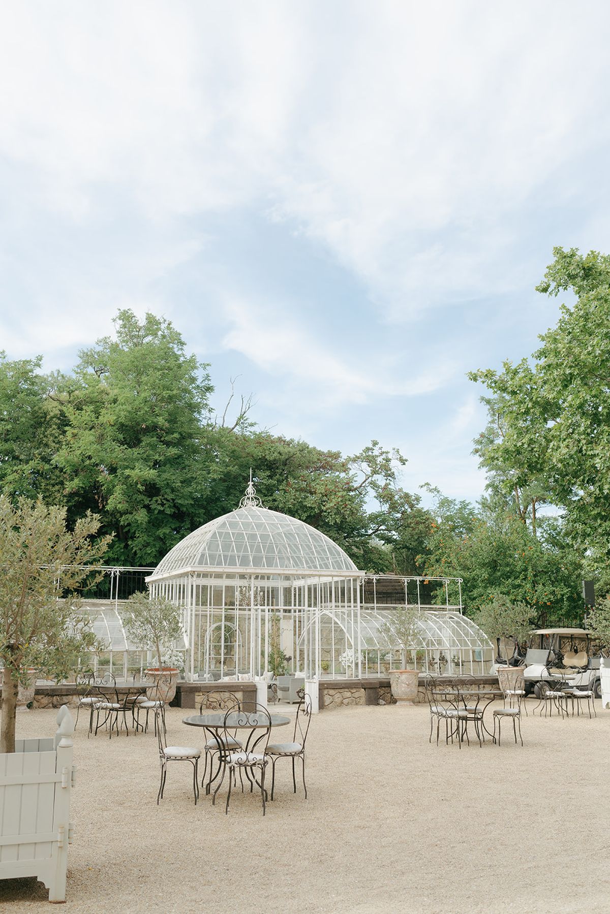 The glass greenhouse and a gravel courtyard with bistro tables at the estate
