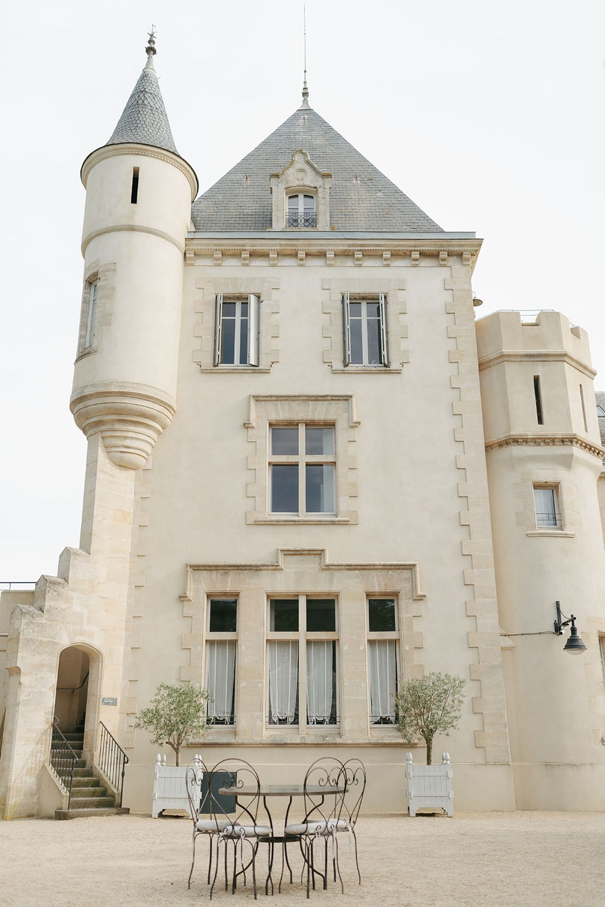 A corner tower and stone façade of Château les Carrasses with a small table and chairs at its foot