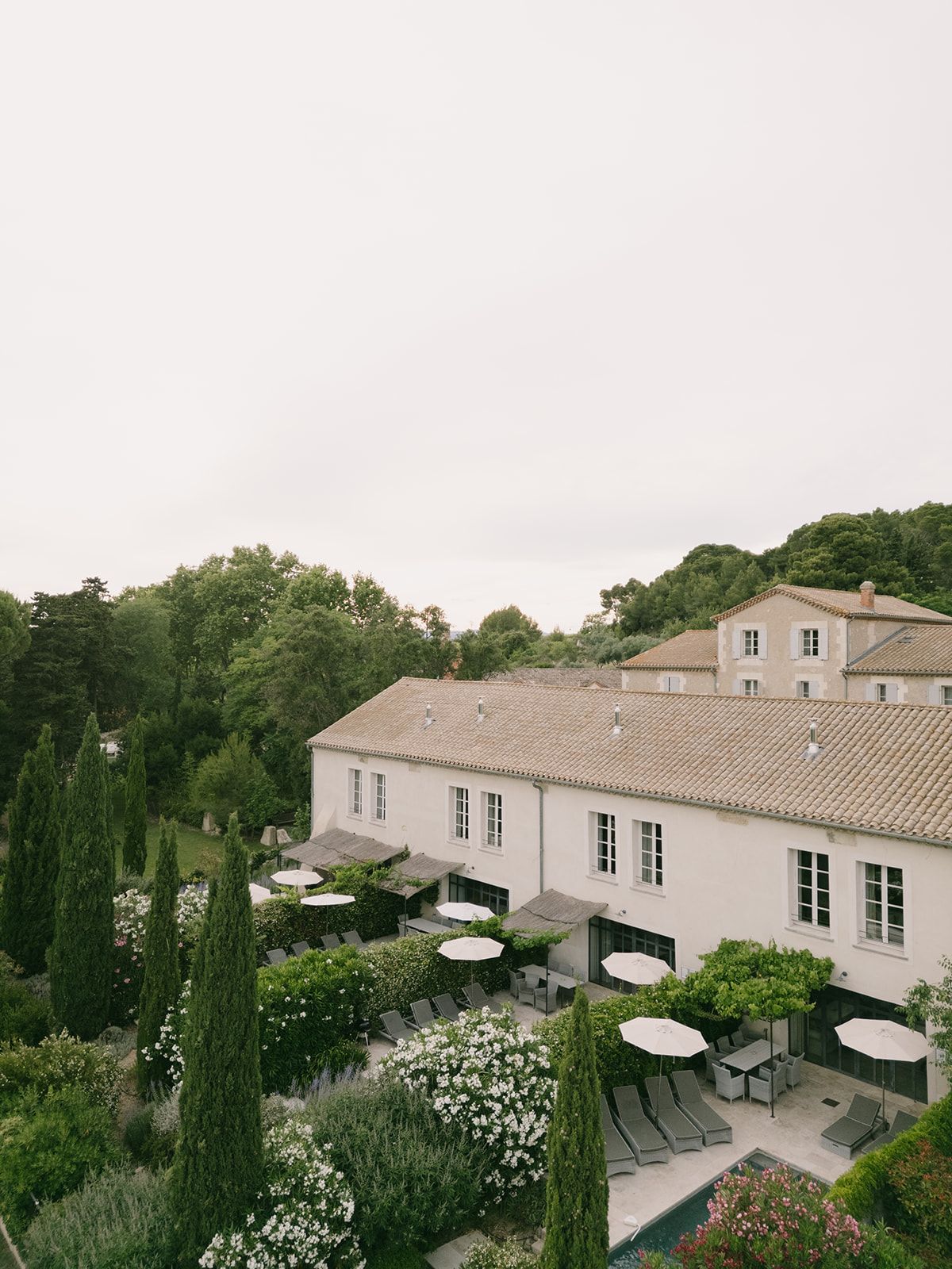 A long stone wing of the estate above gardens of cypress and white flowering shrubs