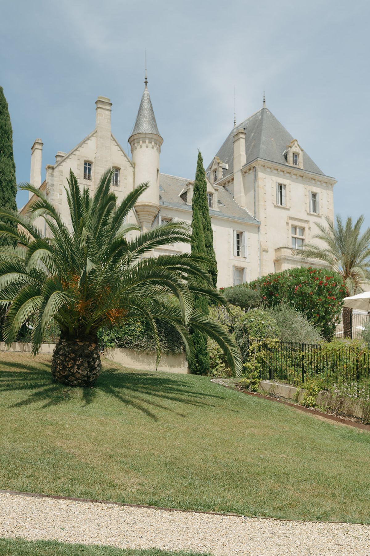 Château les Carrasses seen across a lawn with palm trees and a tall cypress