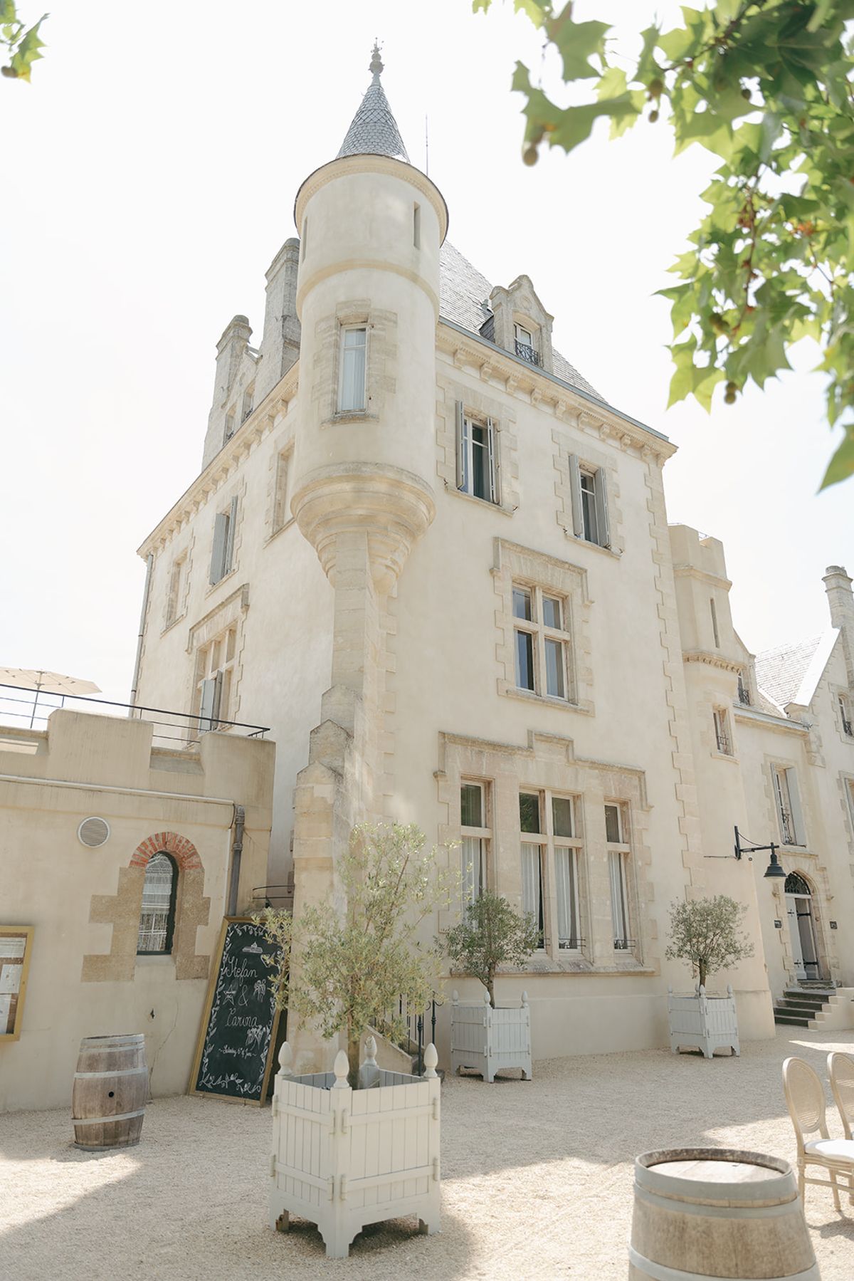 The stone tower of Château les Carrasses with wine barrels and potted olive trees at its base