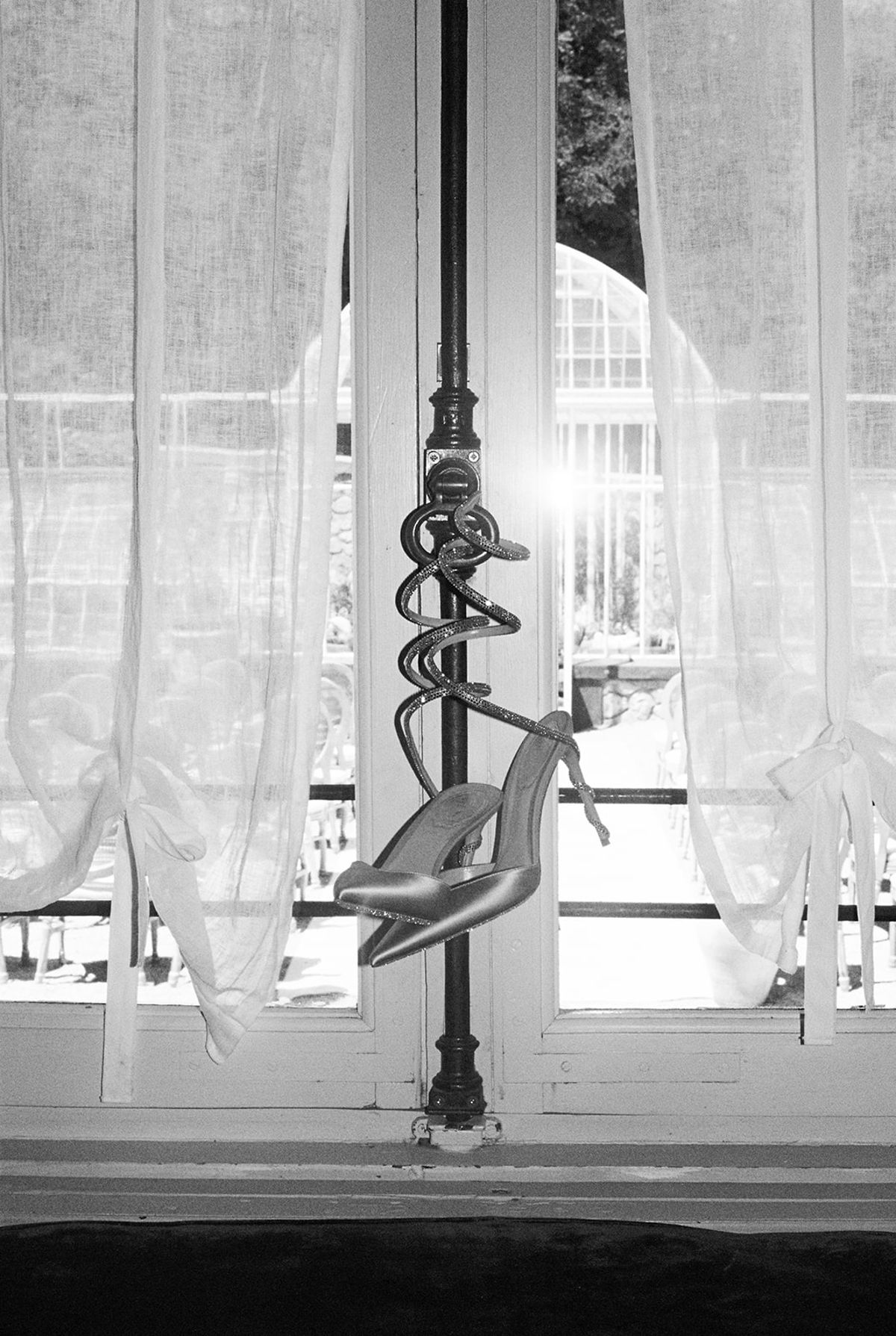 Black and white view of a pair of silver heels hanging from a window latch