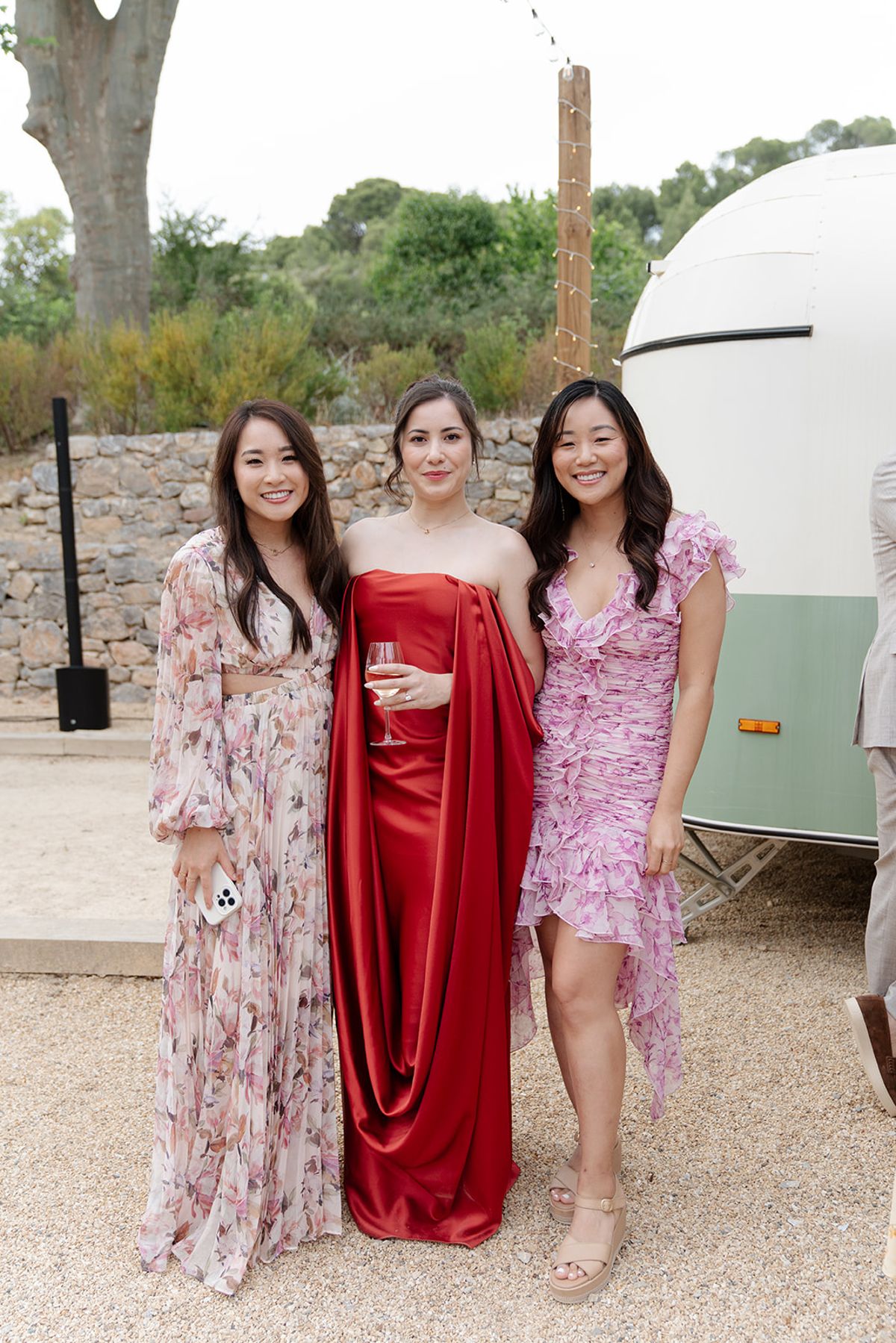 Carina in her red gown with two friends beside the vintage trailer bar at the welcome party the day before