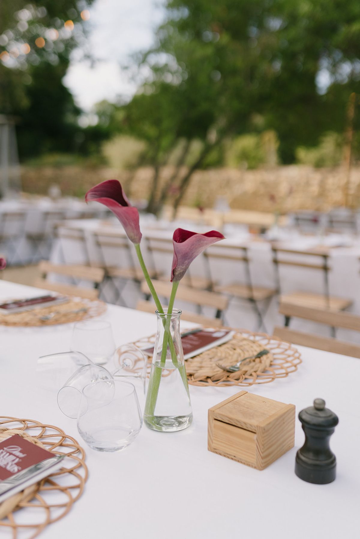 A single burgundy calla lily in a glass bud vase on a table at the welcome party the day before