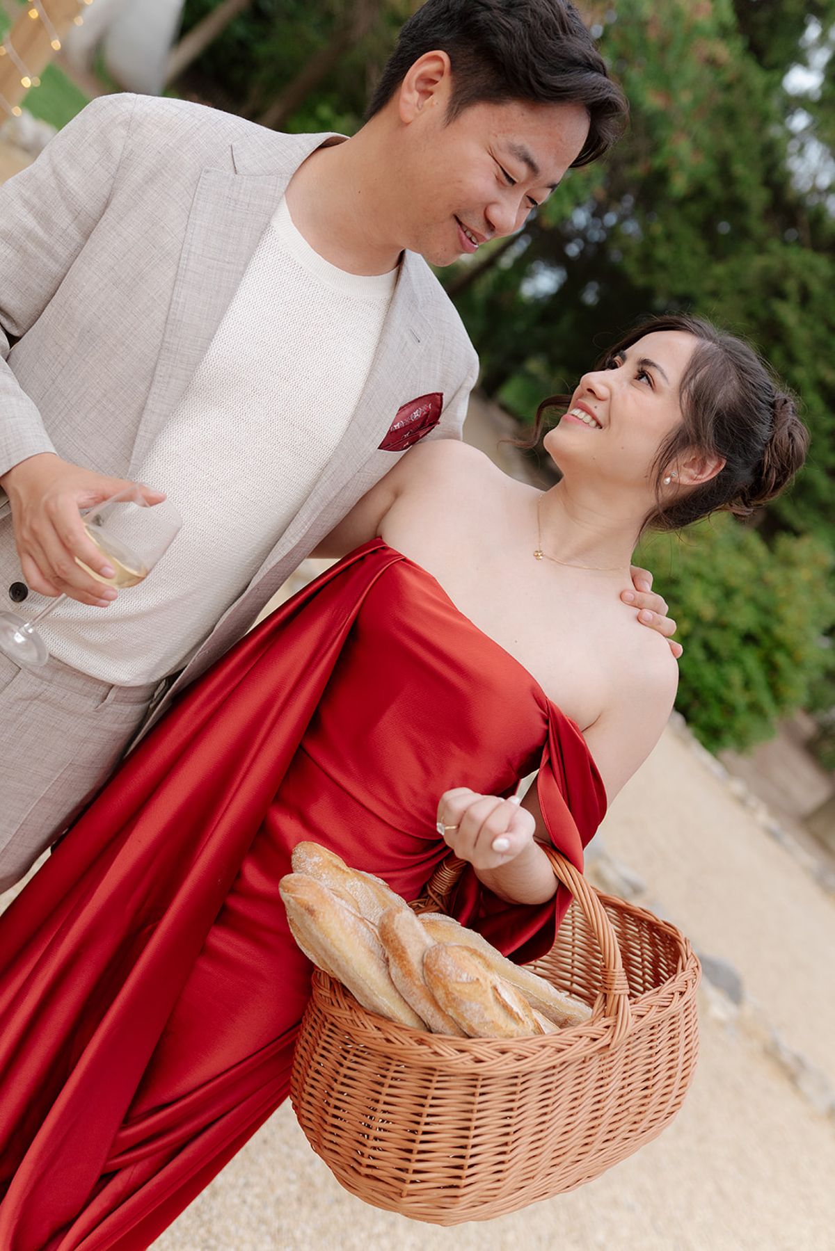 Stefan holding a glass of wine, arm around Carina as she carries baguettes, at the welcome party the day before