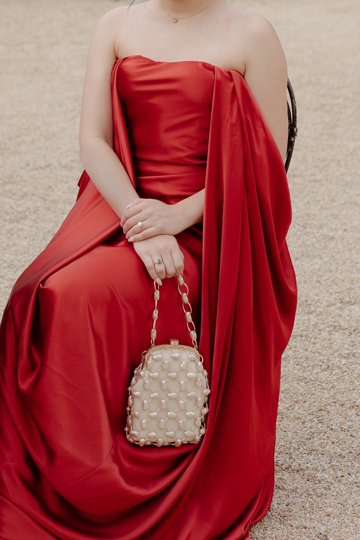 Carina seated in her red satin gown, a pearl-studded clutch on her lap, at the welcome party the day before