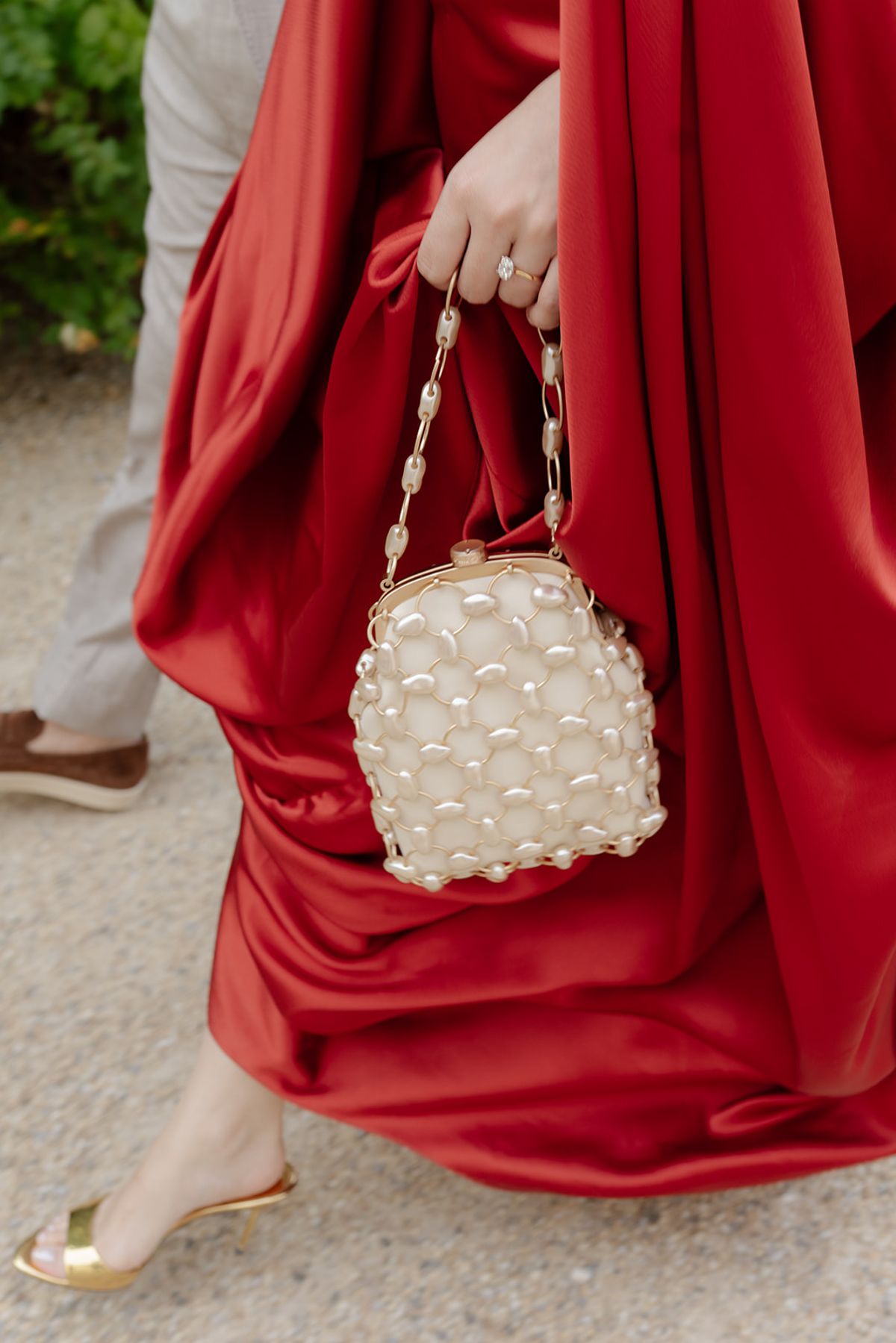 Detail of a draped red satin gown, pearl-studded clutch and gold heel at the welcome party the day before