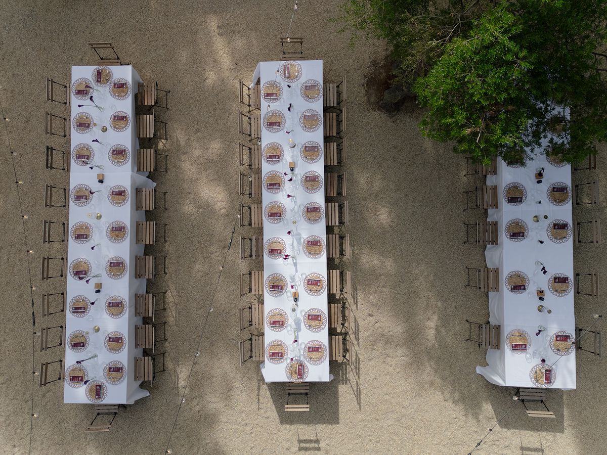 Aerial view of three long tables laid in white on a gravel terrace at the welcome party the day before