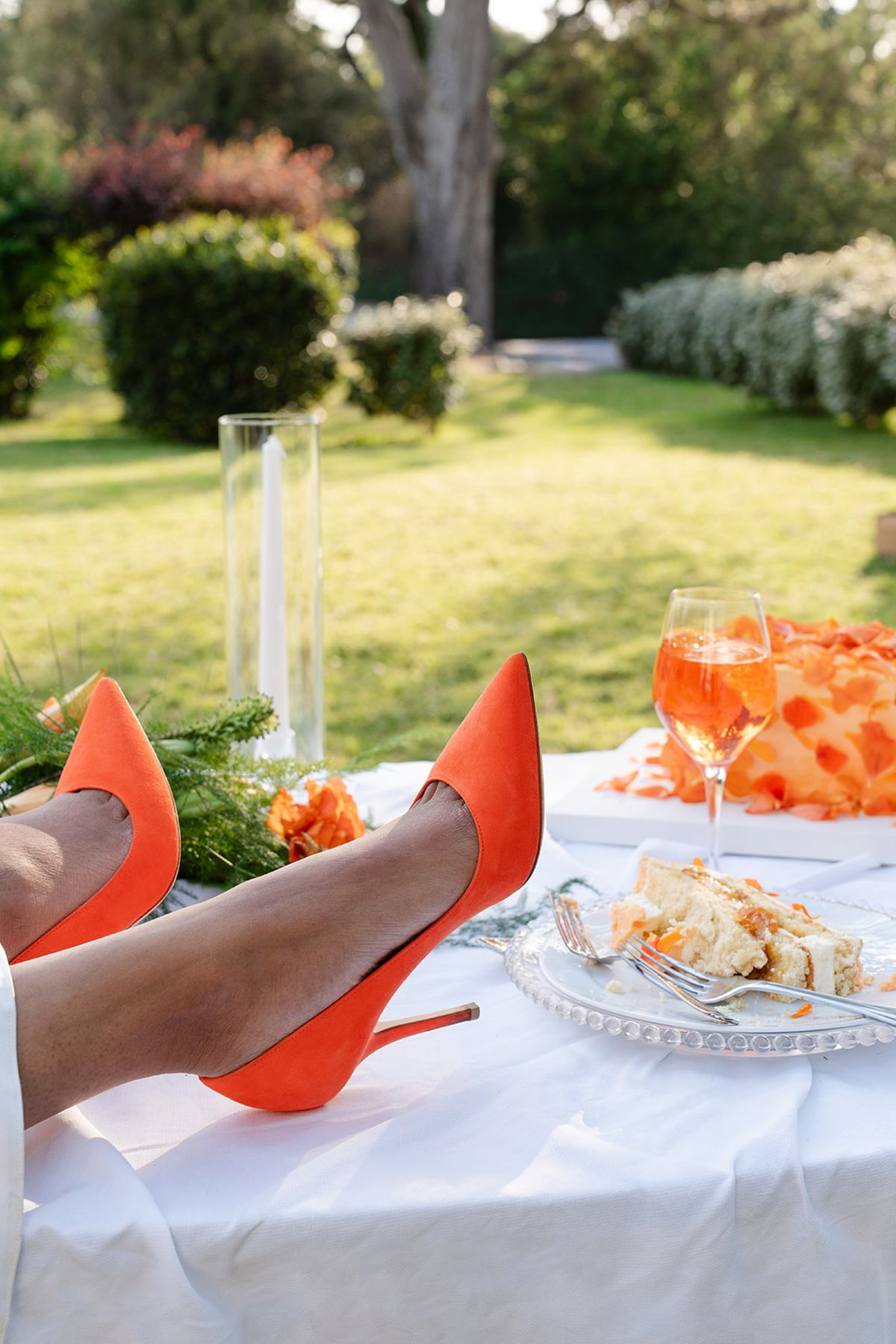 Orange heels resting on the table beside a slice of cake and a glass of spritz