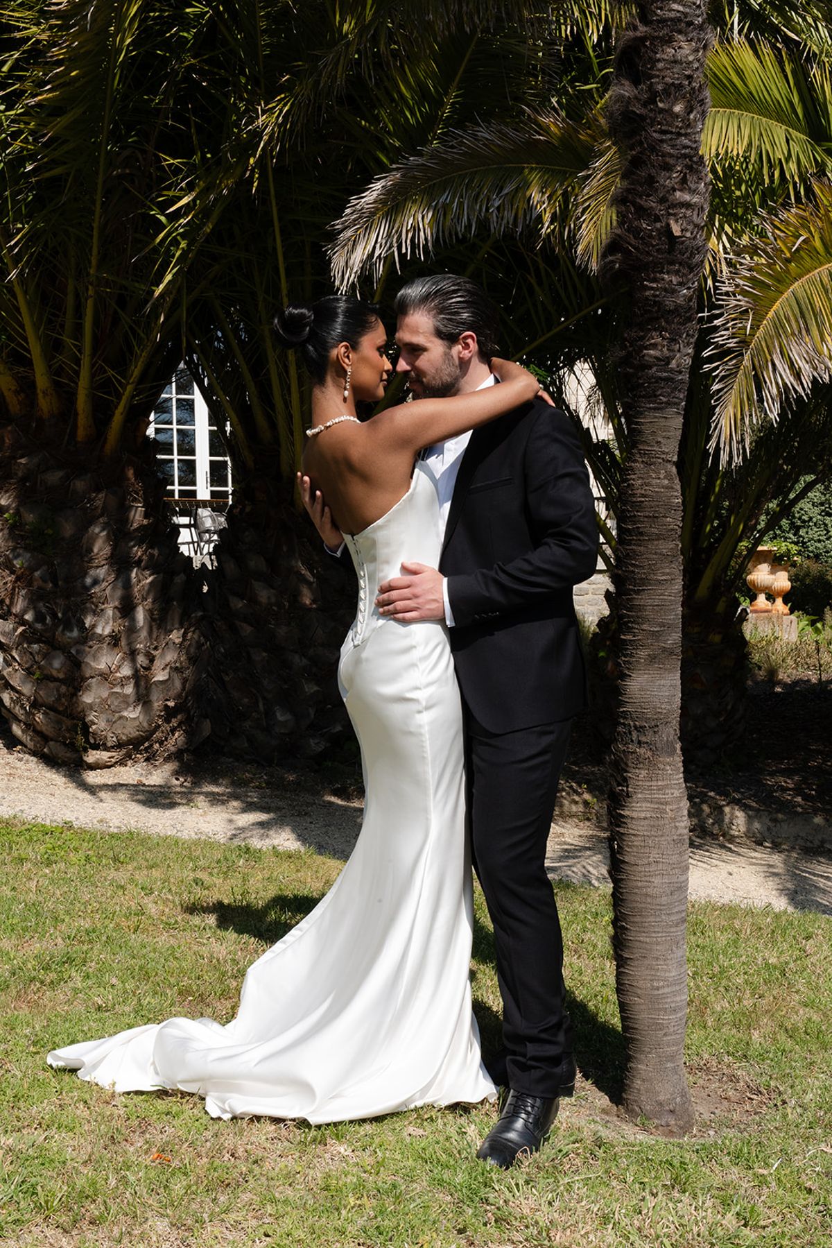 The bride and groom embrace beneath a palm tree in the villa's gardens