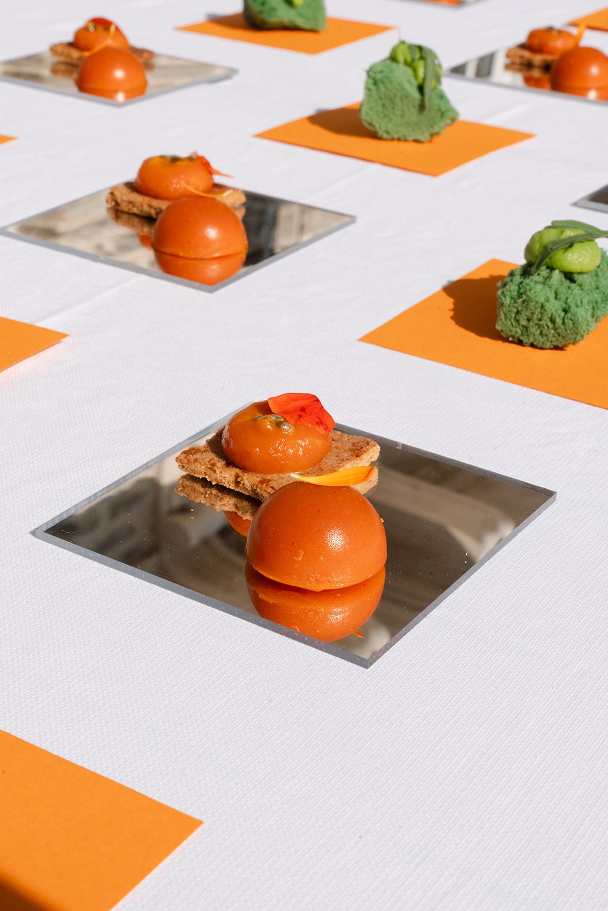 Canapés on mirrored tiles alternating with orange napkins on a white table