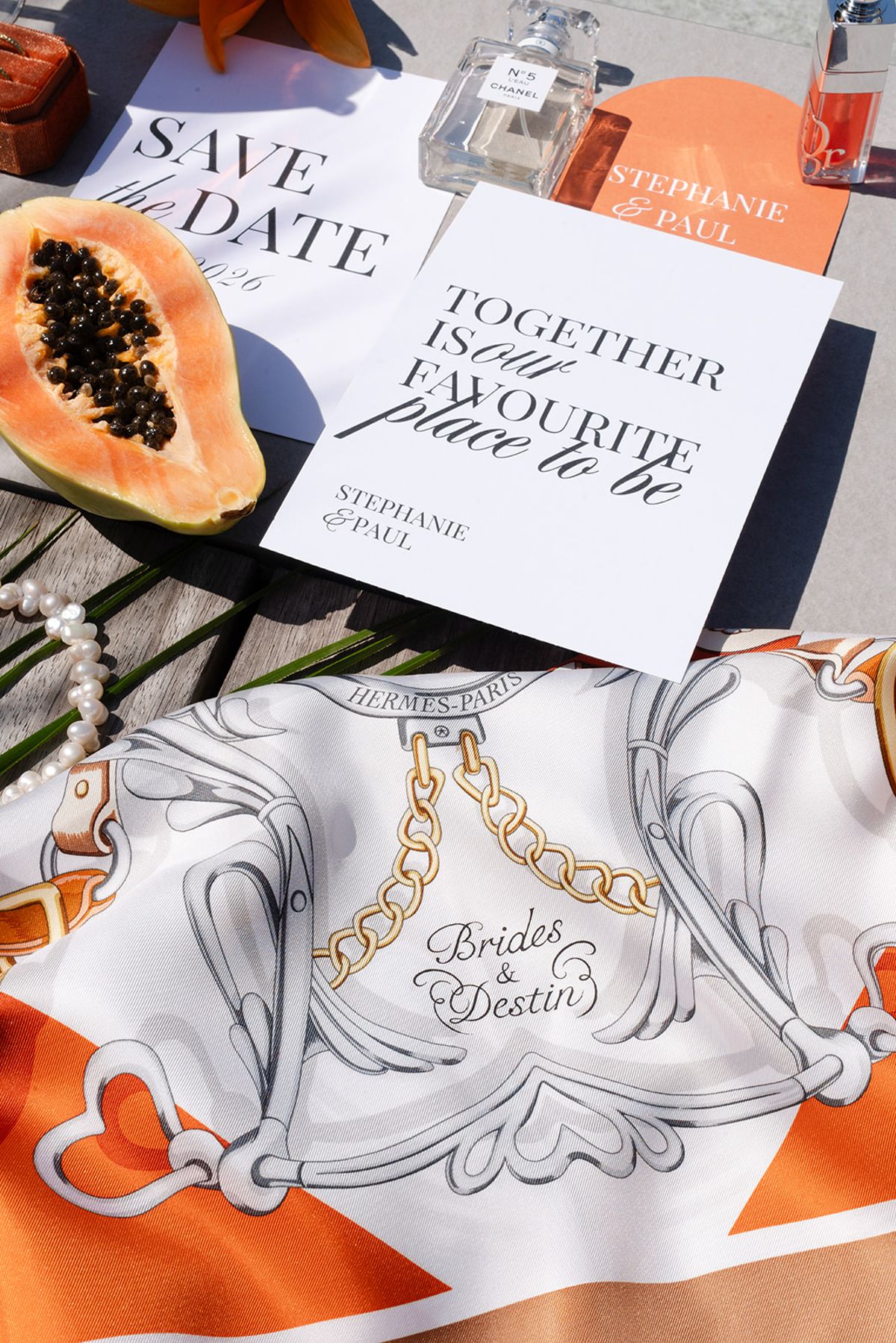Save-the-date and stationery for Stéphanie and Paul laid on an orange Hermès scarf with a papaya and pearls