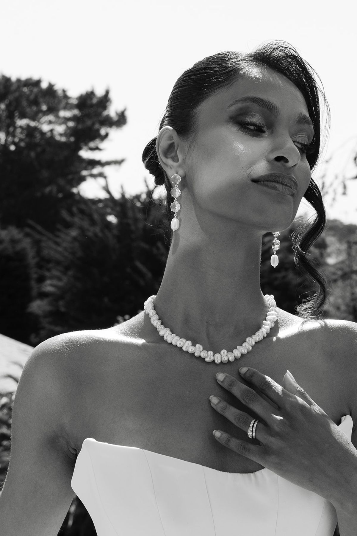 Black and white portrait of the bride in pearl drop earrings and a pearl necklace, one hand at her collarbone