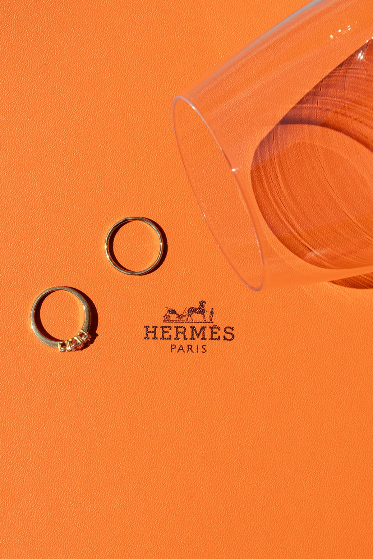 Two wedding rings on an orange Hermès box beside an upturned glass