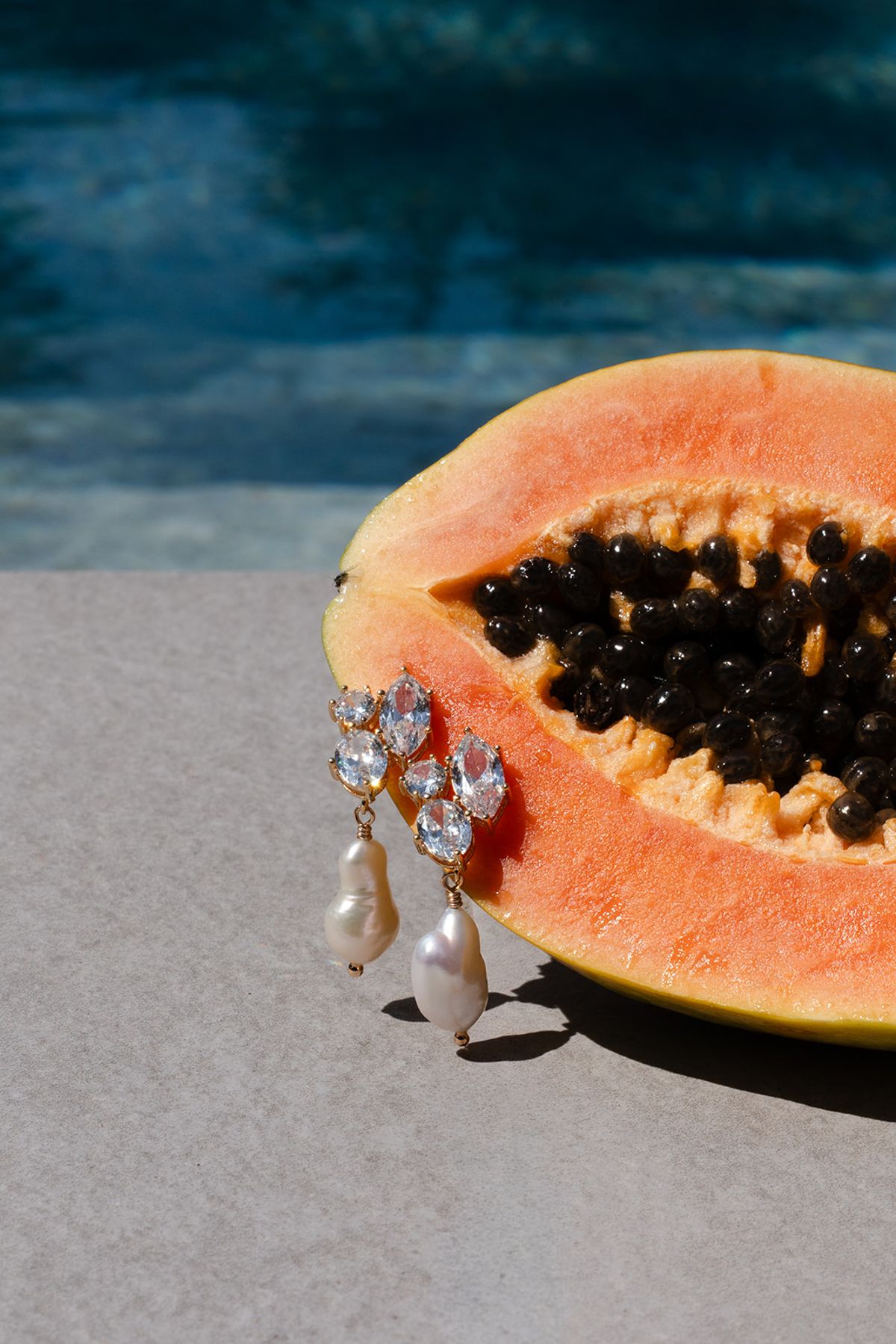 Half a papaya holding a pearl drop earring beside the swimming pool