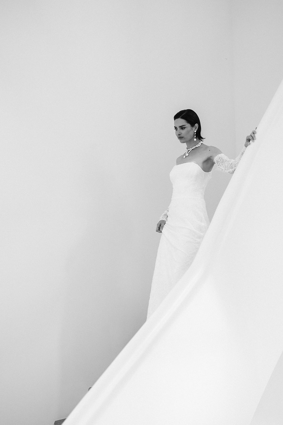 The bride descends a curved white staircase in her gown, one hand trailing the banister.