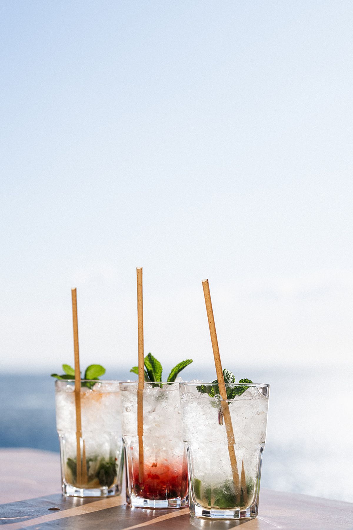 Three crushed-ice cocktails garnished with mint stand in a row on a table above the sea.