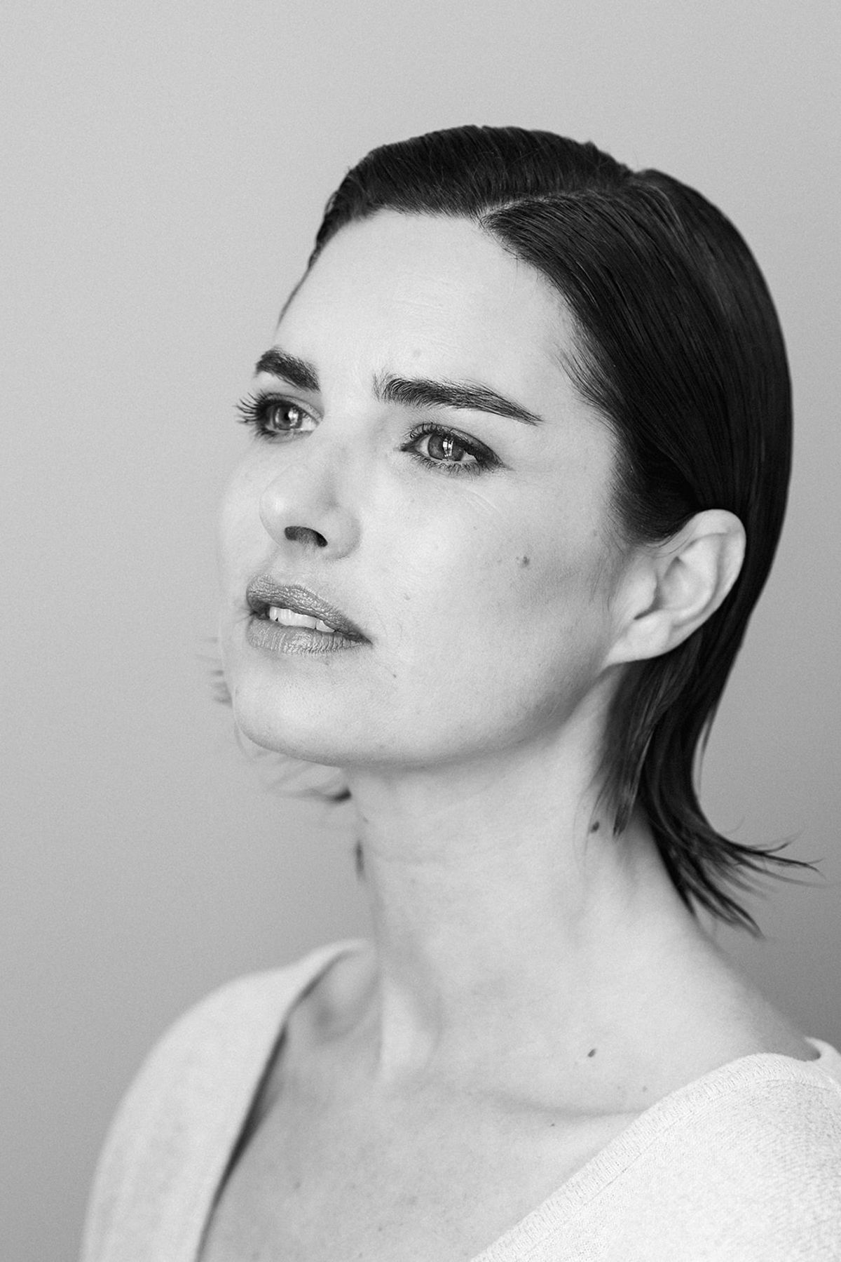 A close black-and-white portrait of the bride mid-preparation, hair pulled back and expression composed.