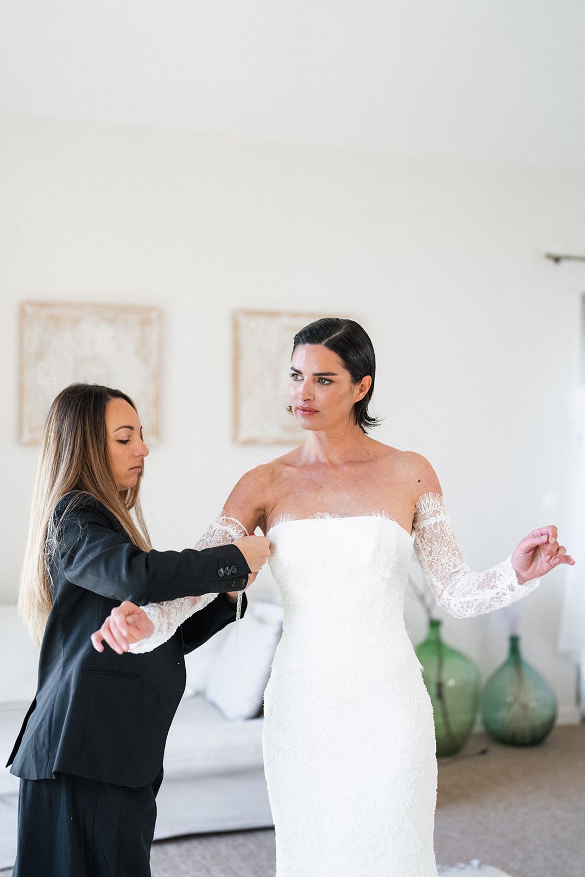 A stylist laces the back of the bride’s gown as she stands in the getting-ready suite.