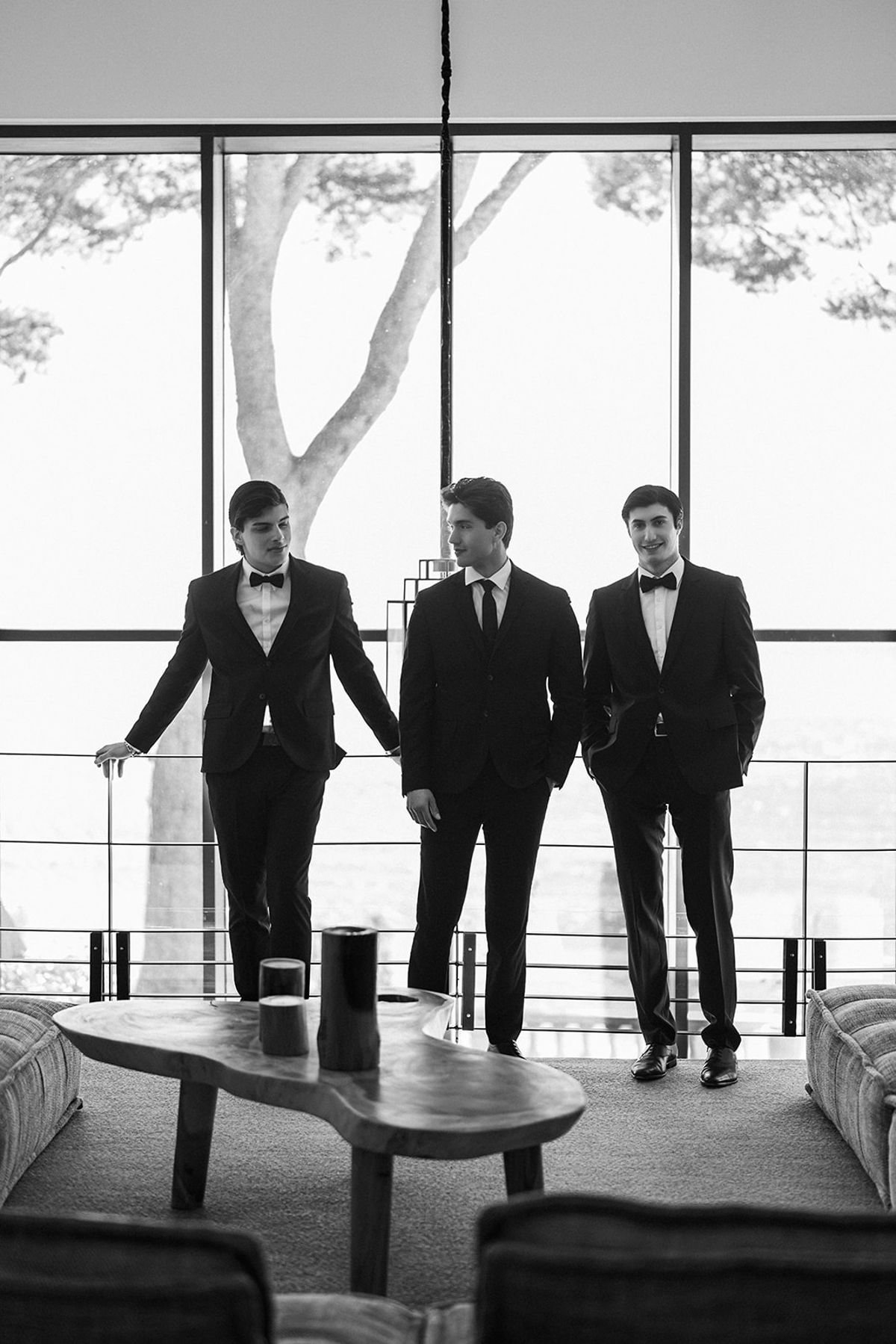 Three groomsmen in black tie pose together outside the estate.