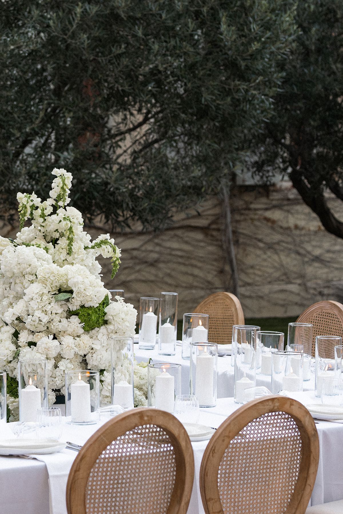 Close detail of the reception table: pillar candles in glass hurricanes beside a tall white floral arrangement.