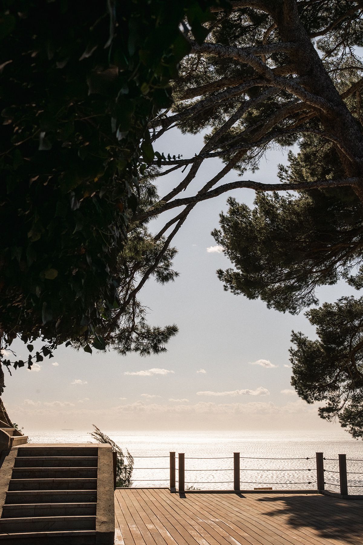 A tiered white floral installation on a stone pedestal stands at the edge of the ceremony deck, the sea beyond.