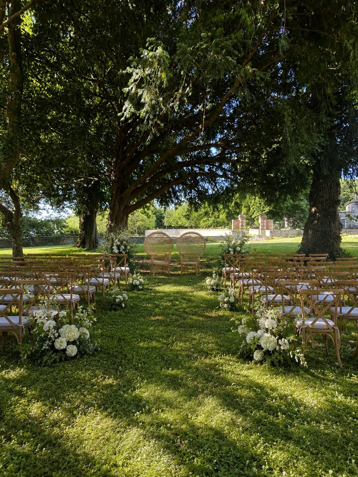 Outdoor ceremony set beneath mature trees, with wooden chairs and white florals