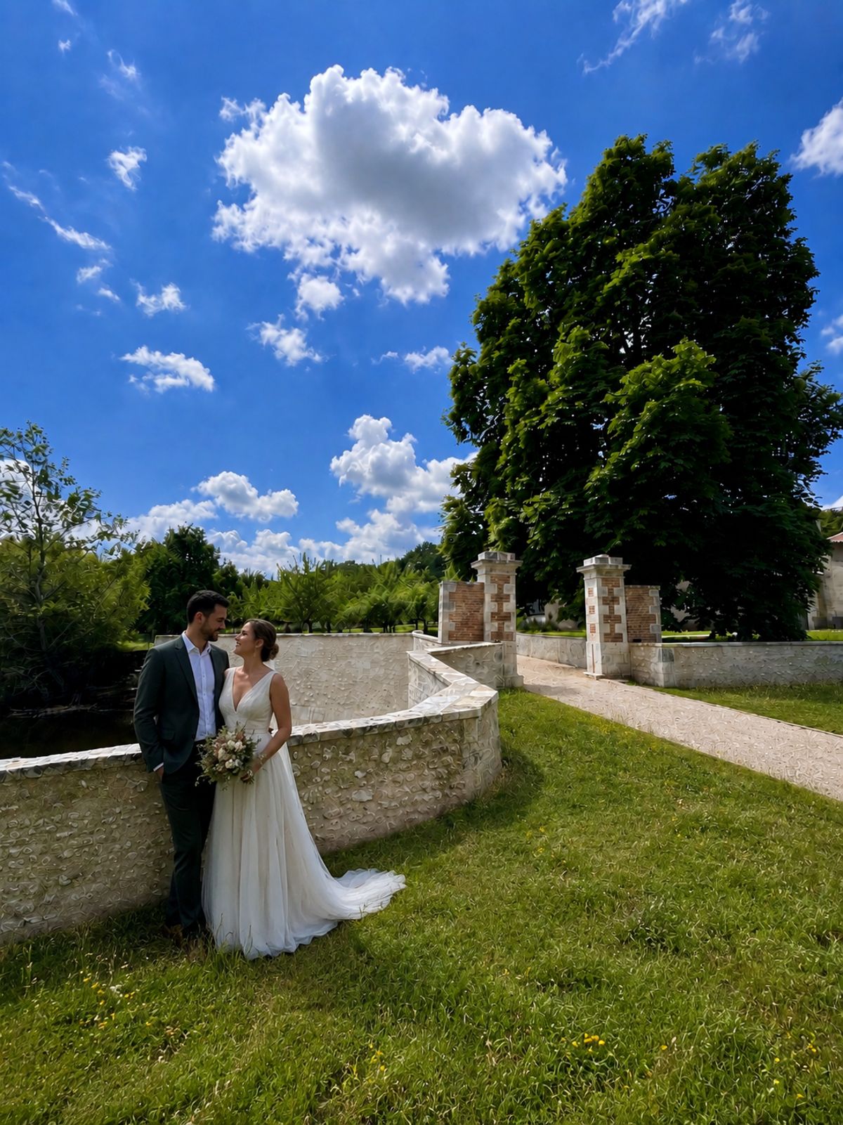 A couple beside the curved stone wall in the grounds at Château de la Faye