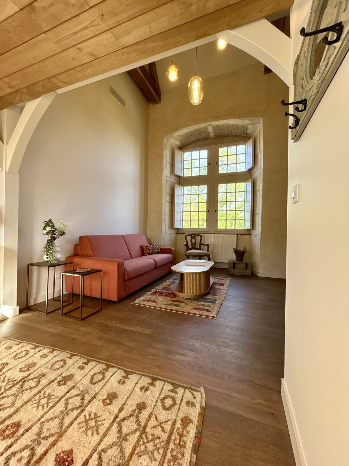 Sitting room under a beamed vaulted ceiling, with a coral sofa and stone window