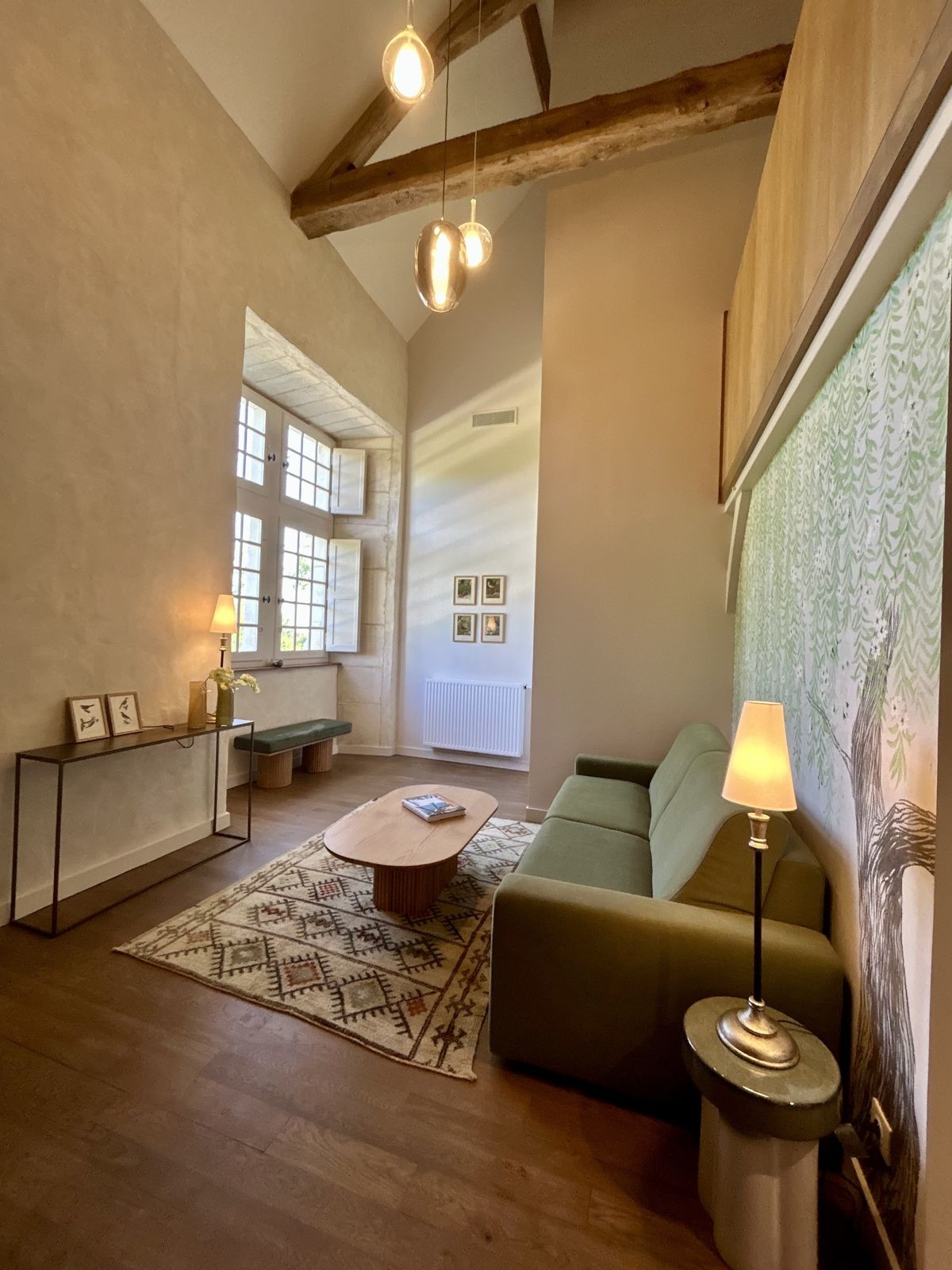 Tall sitting room with a green sofa, painted tree mural and beamed ceiling