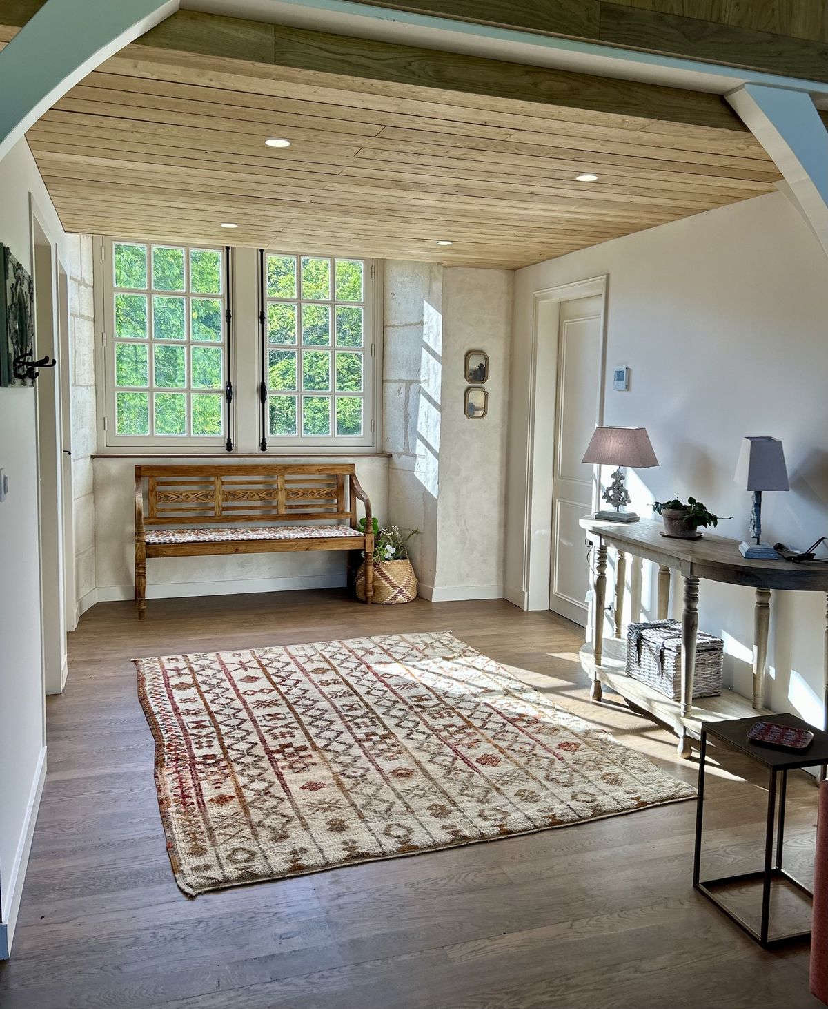 Entrance hall with a wooden bench, patterned rug and tall shuttered windows